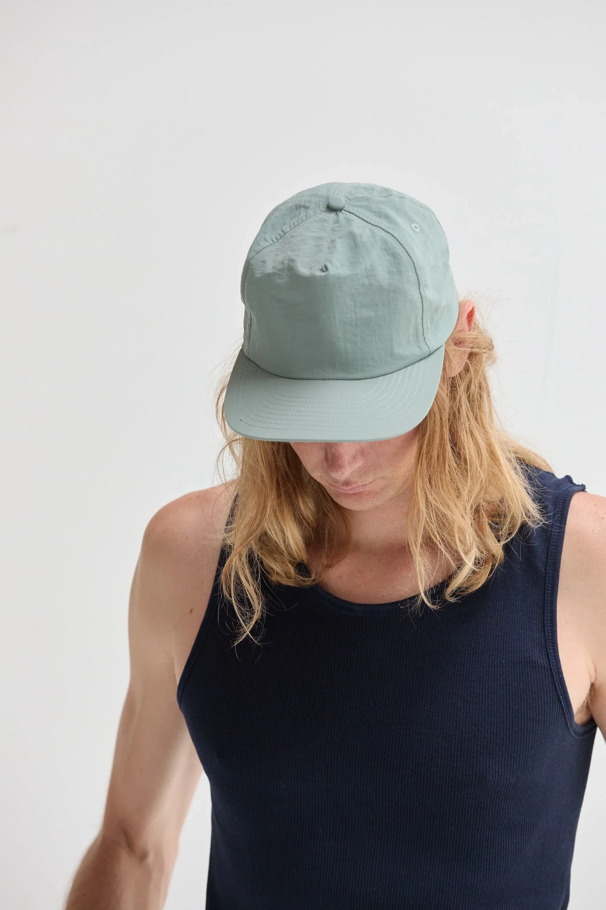 Person in light blue cap and navy tank top, minimalist background, Qu!rk Boutique style