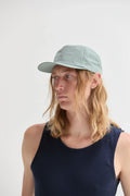 Person with long blond hair in a light blue cap and navy tank top, minimalist style