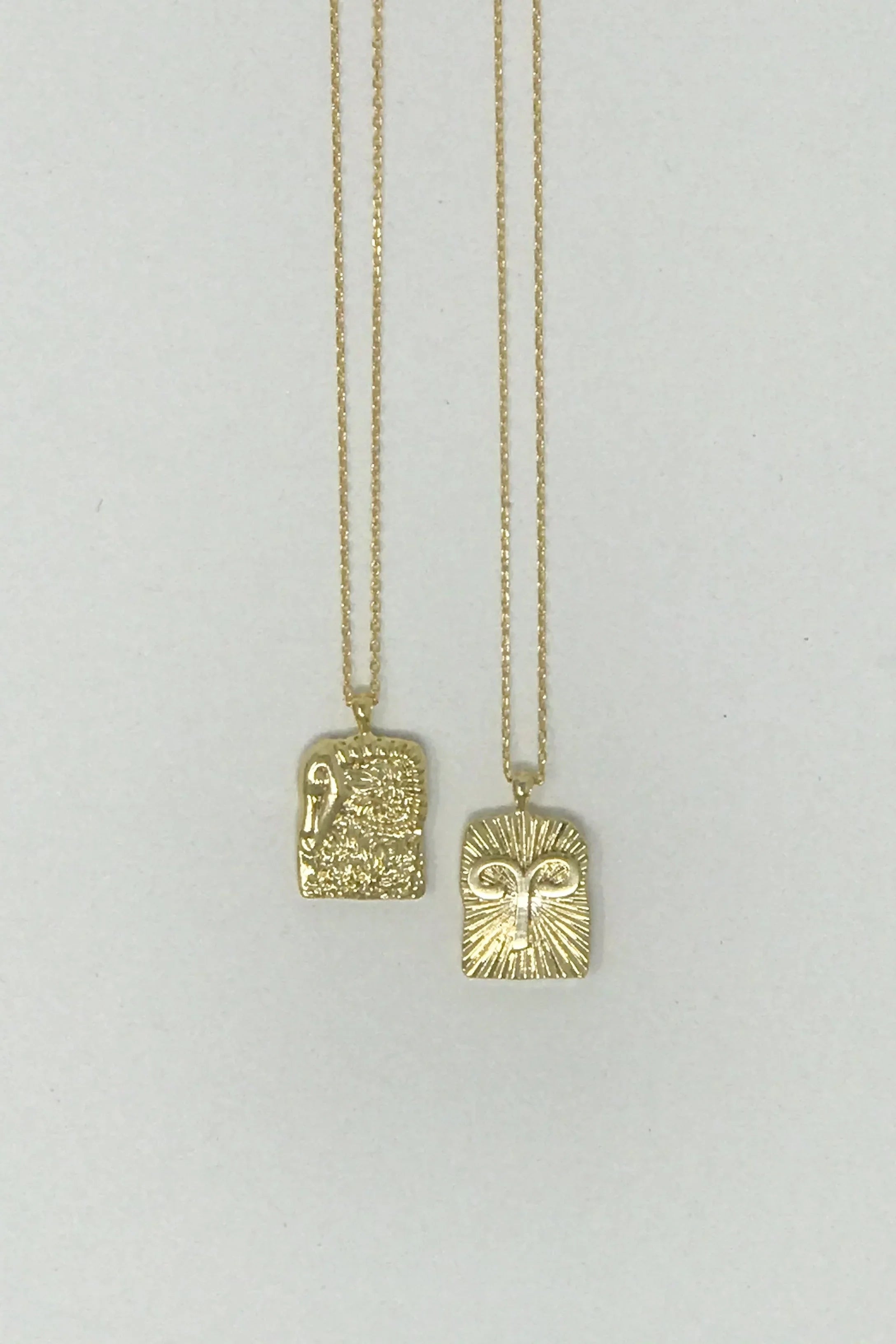 Two gold pendant necklaces with textured rectangular charms on thin chains