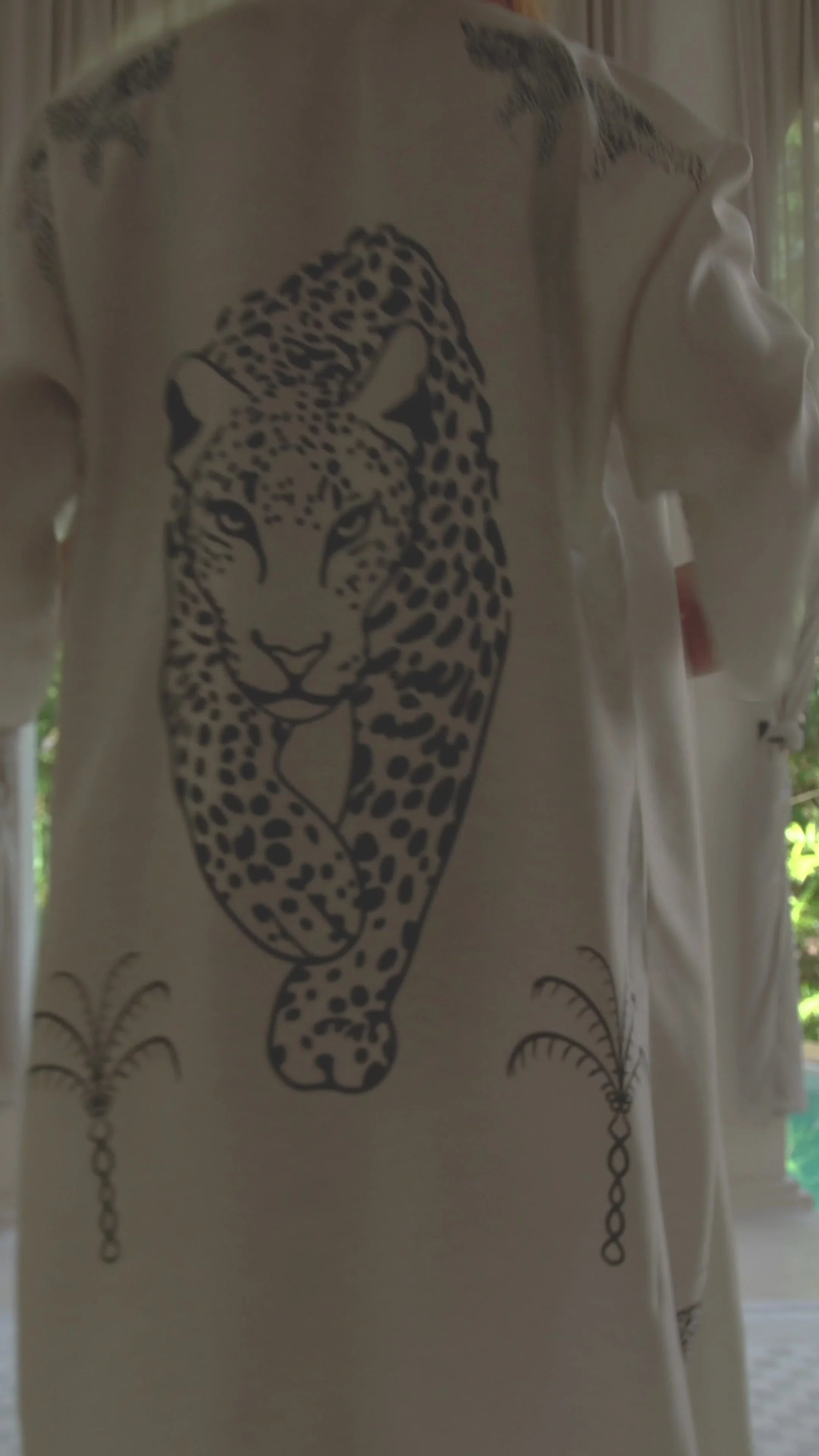 White garment with a large black leopard print and small palm tree designs on sleeves and front
