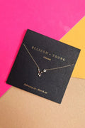 Ellison + Young Pisces constellation necklace on black card with gold lettering, pink and yellow background