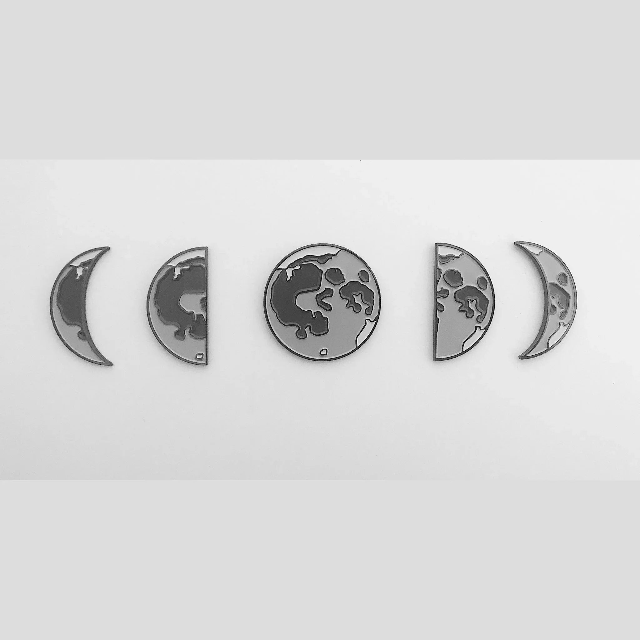 Set of enamel pins depicting moon phases in gray tones on a white background