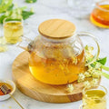 Glass teapot with herbal tea and blossoms, on wooden tray, eco-friendly boutique style