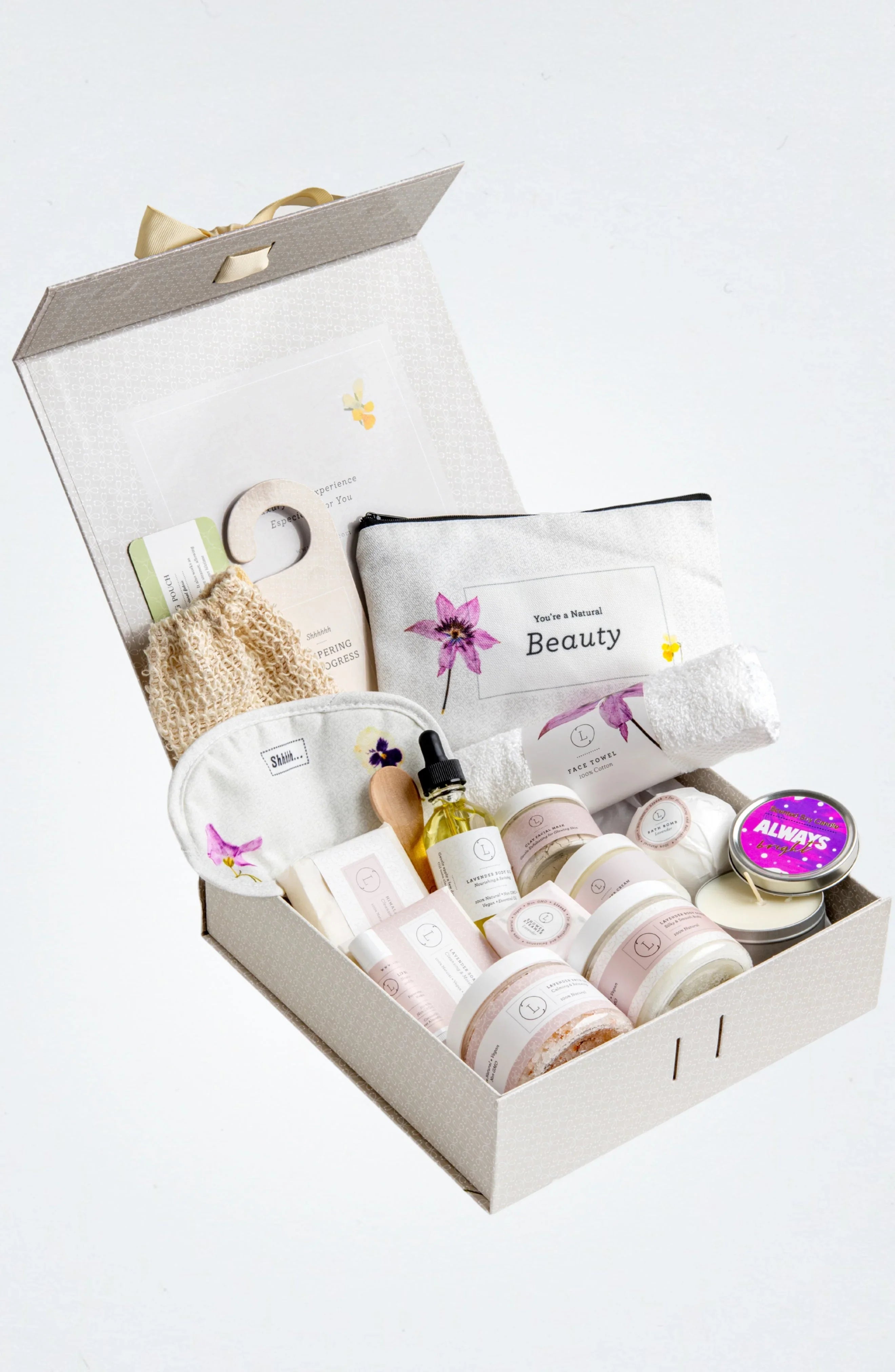 Open spa gift box with skincare products, lavender body oil, bath salts, towel, and candle