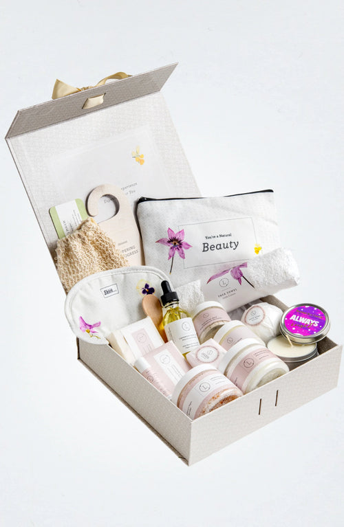 Open spa gift box with skincare products, lavender body oil, bath salts, towel, and candle