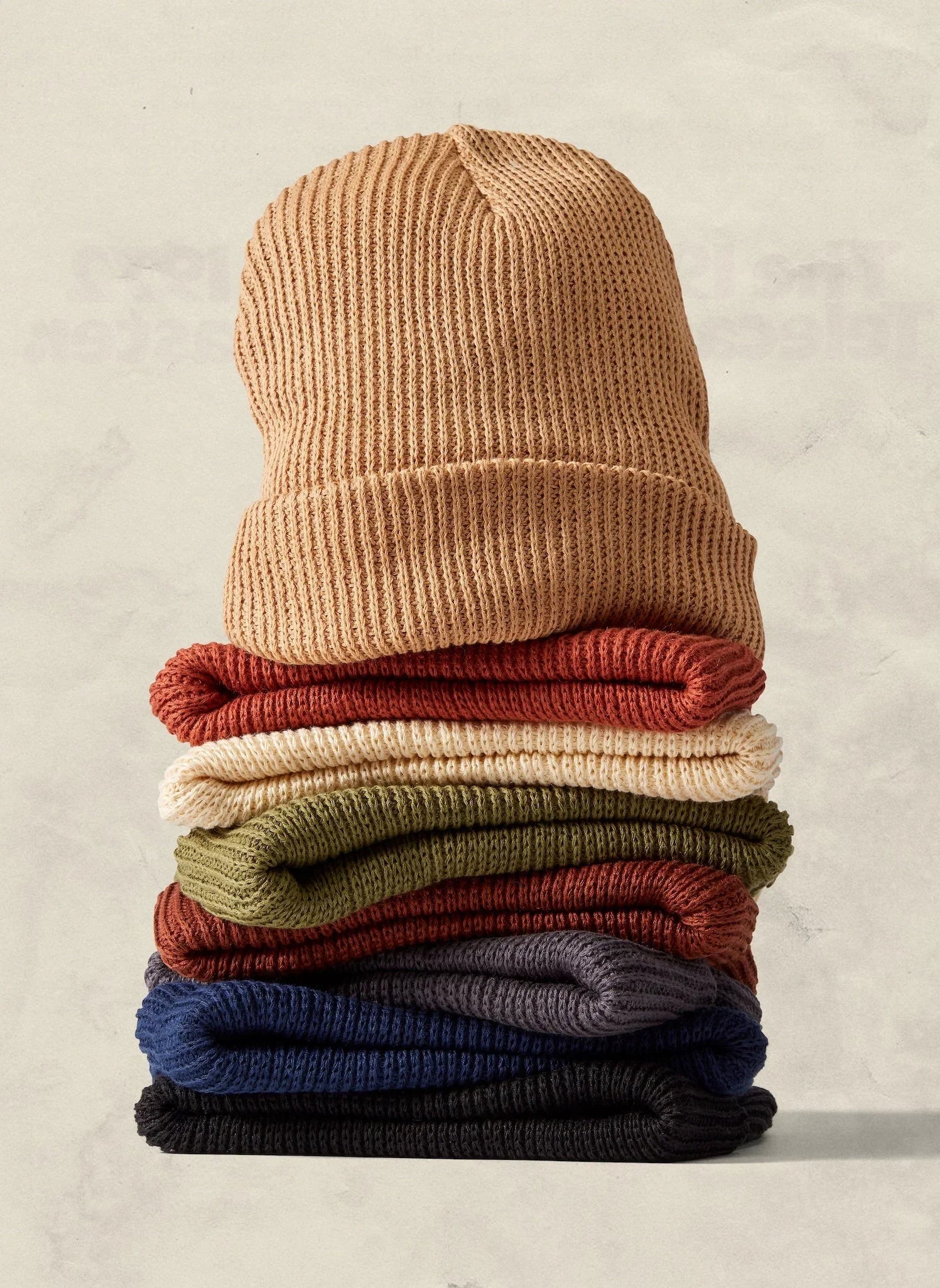 Stack of colorful knit beanies in earthy tones, cozy winter hats at Qu!rk Boutique