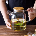 Glass teapot with bamboo lid, filled with lemon and mint herbal tea, on wooden table