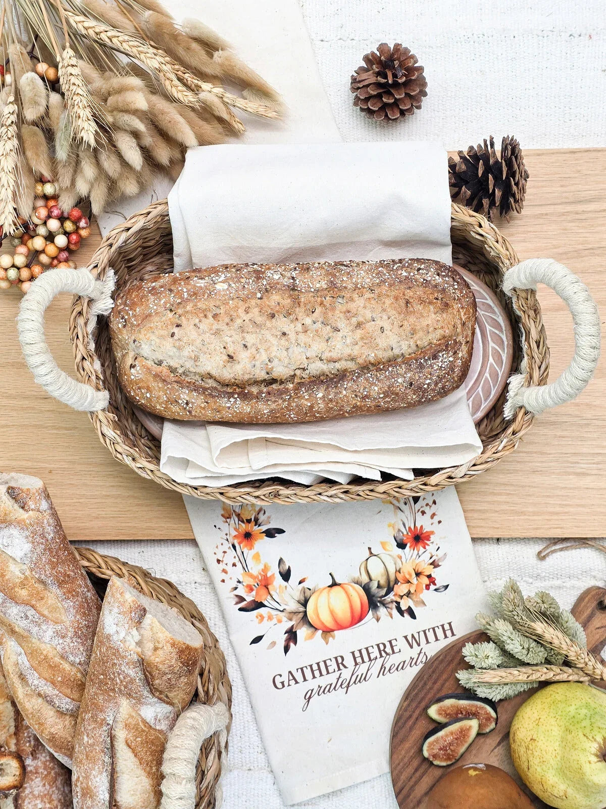 Whole grain bread in woven basket with autumn decor and 'Gather Here With Grateful Hearts' towel