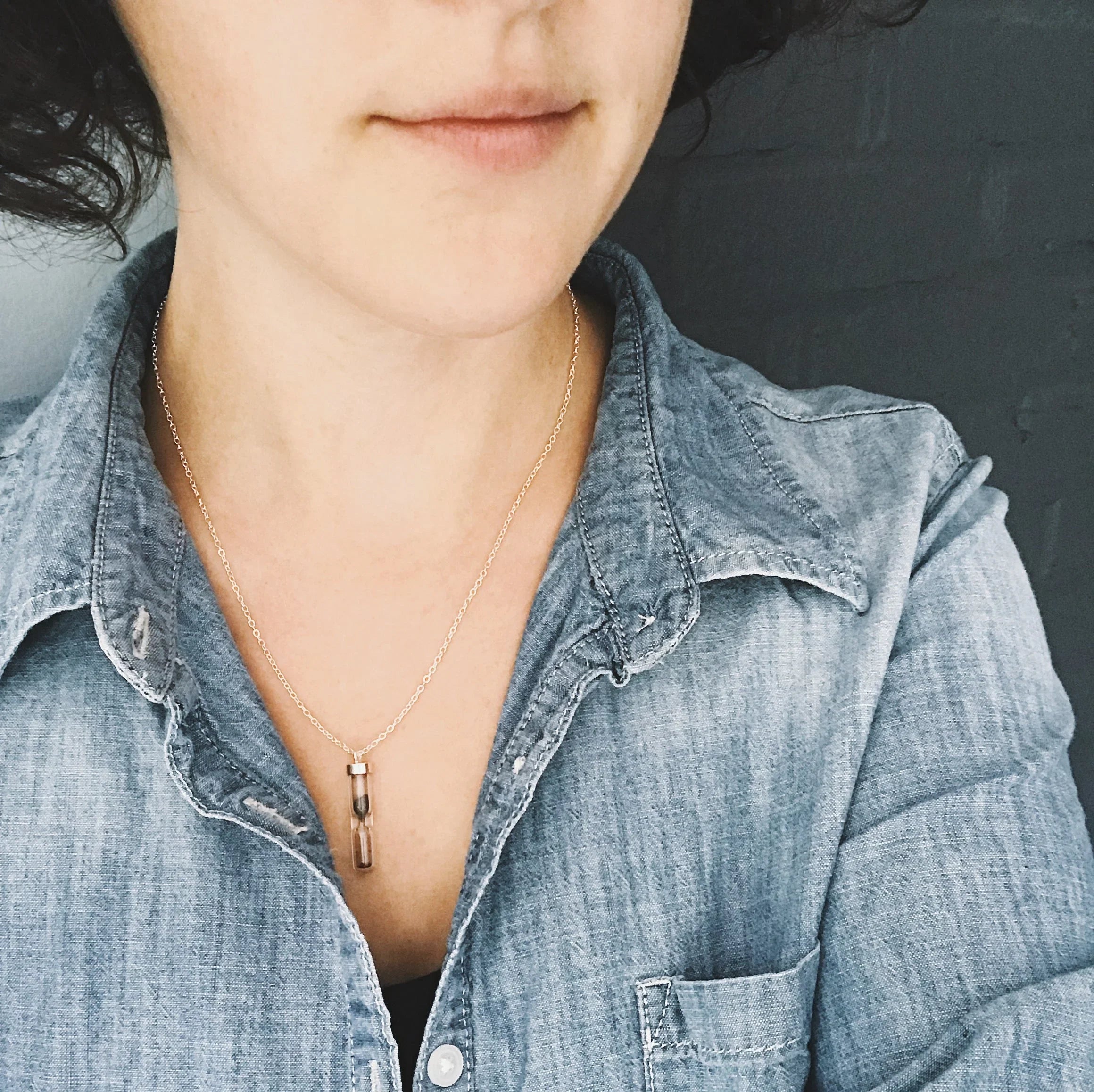 Close-up of woman wearing an hourglass pendant necklace with a denim shirt on gray background