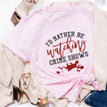Pink t-shirt with black and red text 'I'd rather be watching crime shows' and blood splatter design, styled with beige knitwear and rose gold heels