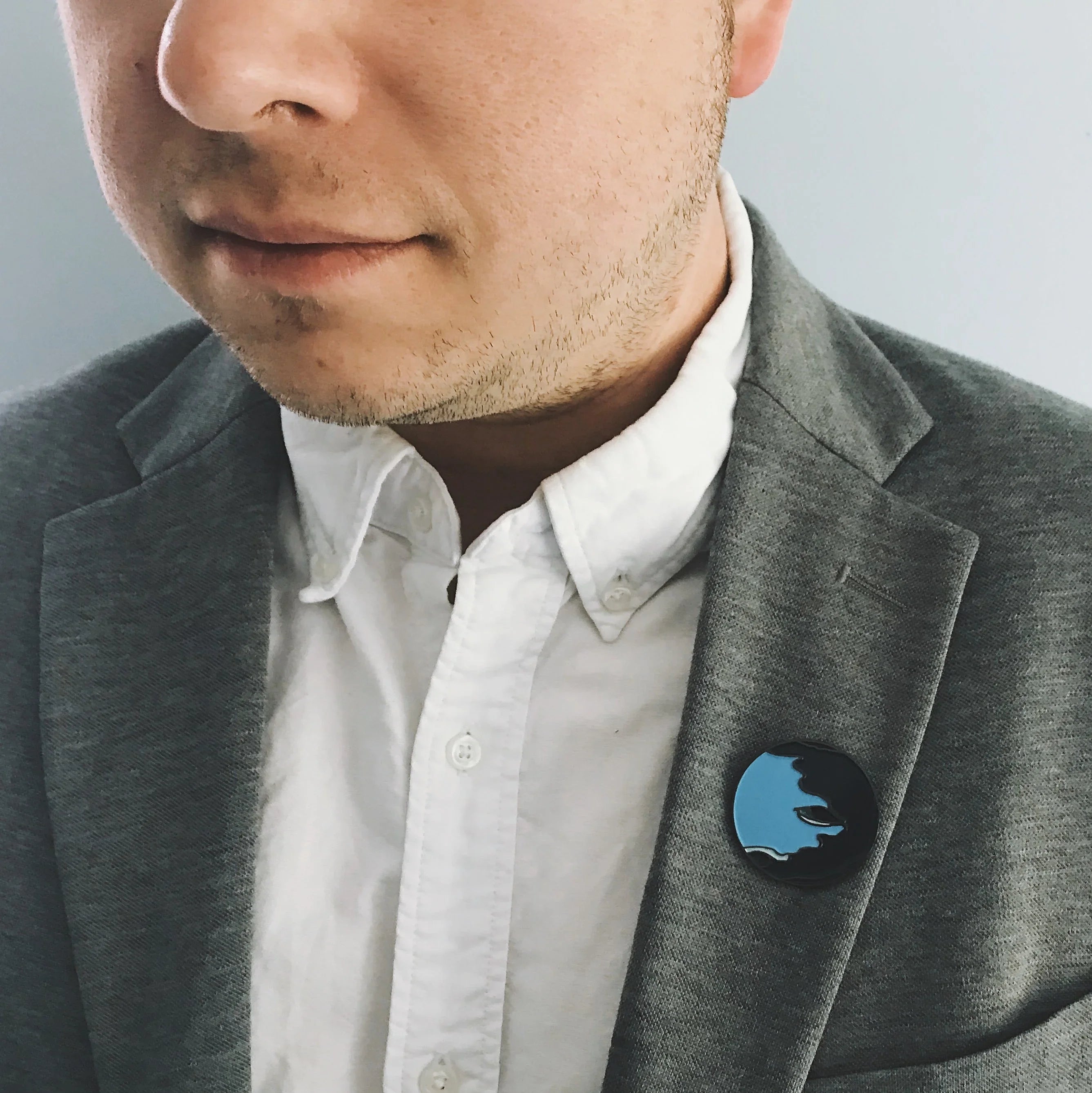Man in grey blazer and white shirt wearing artist-designed black and blue enamel pin badge