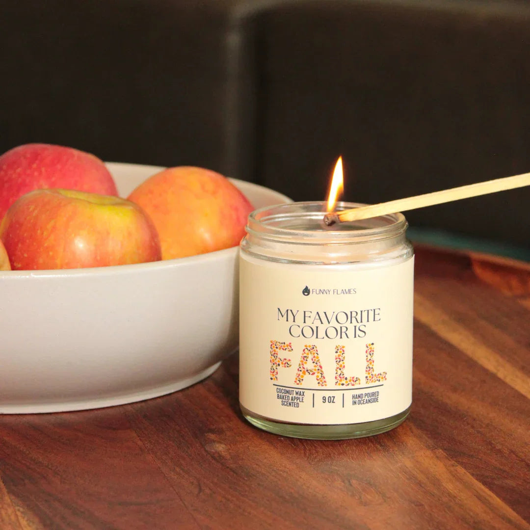 Lit coconut wax candle with fall theme next to a bowl of red apples on wooden table
