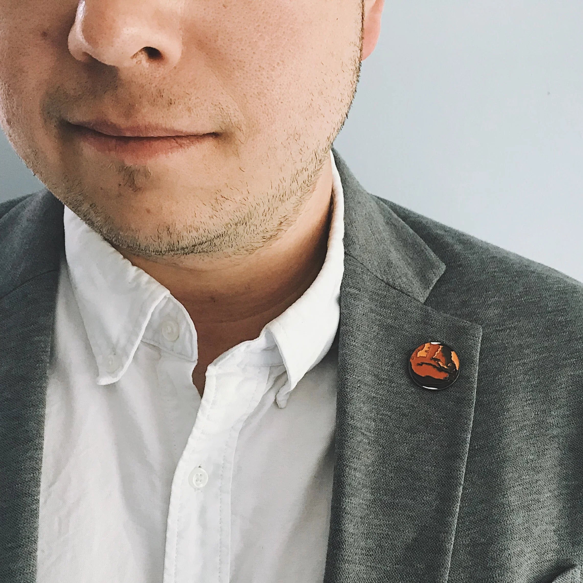 Close-up of man in gray blazer and white shirt wearing round orange and black lapel pin
