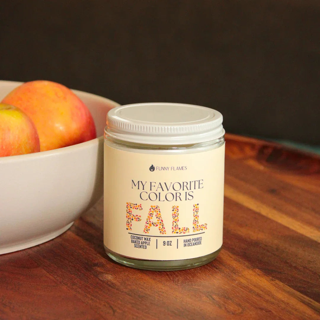 9 oz Funny Flames fall scented candle with baked apple coconut wax on wooden surface near bowl of apples
