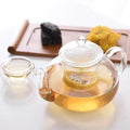 Clear glass teapot with blooming tea, matching glass cup, and snacks on wooden tray