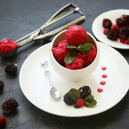 Bowl of berry sorbet garnished with mint, fresh blackberries and raspberries on white plate