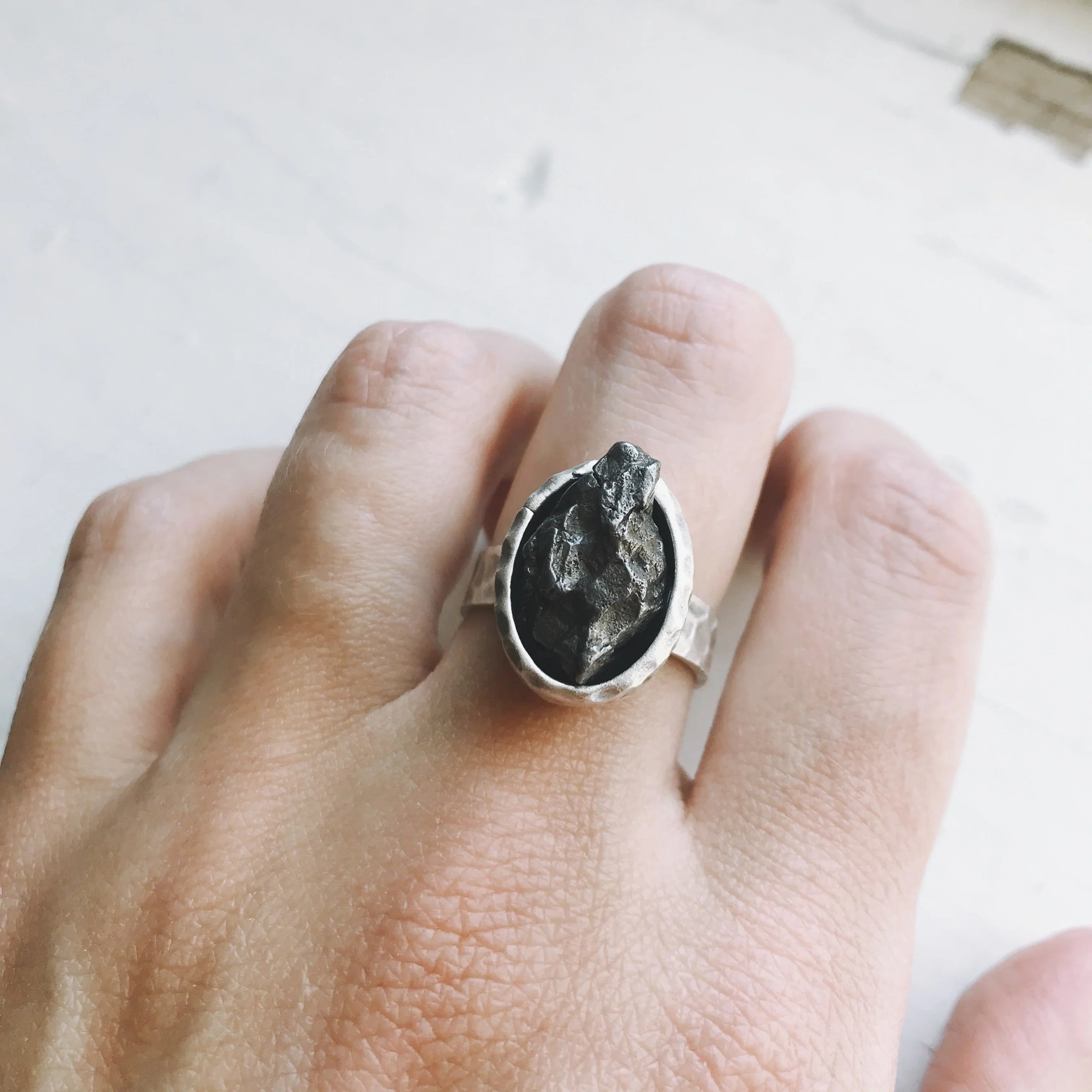 Silver ring with rough black stone on finger against white background
