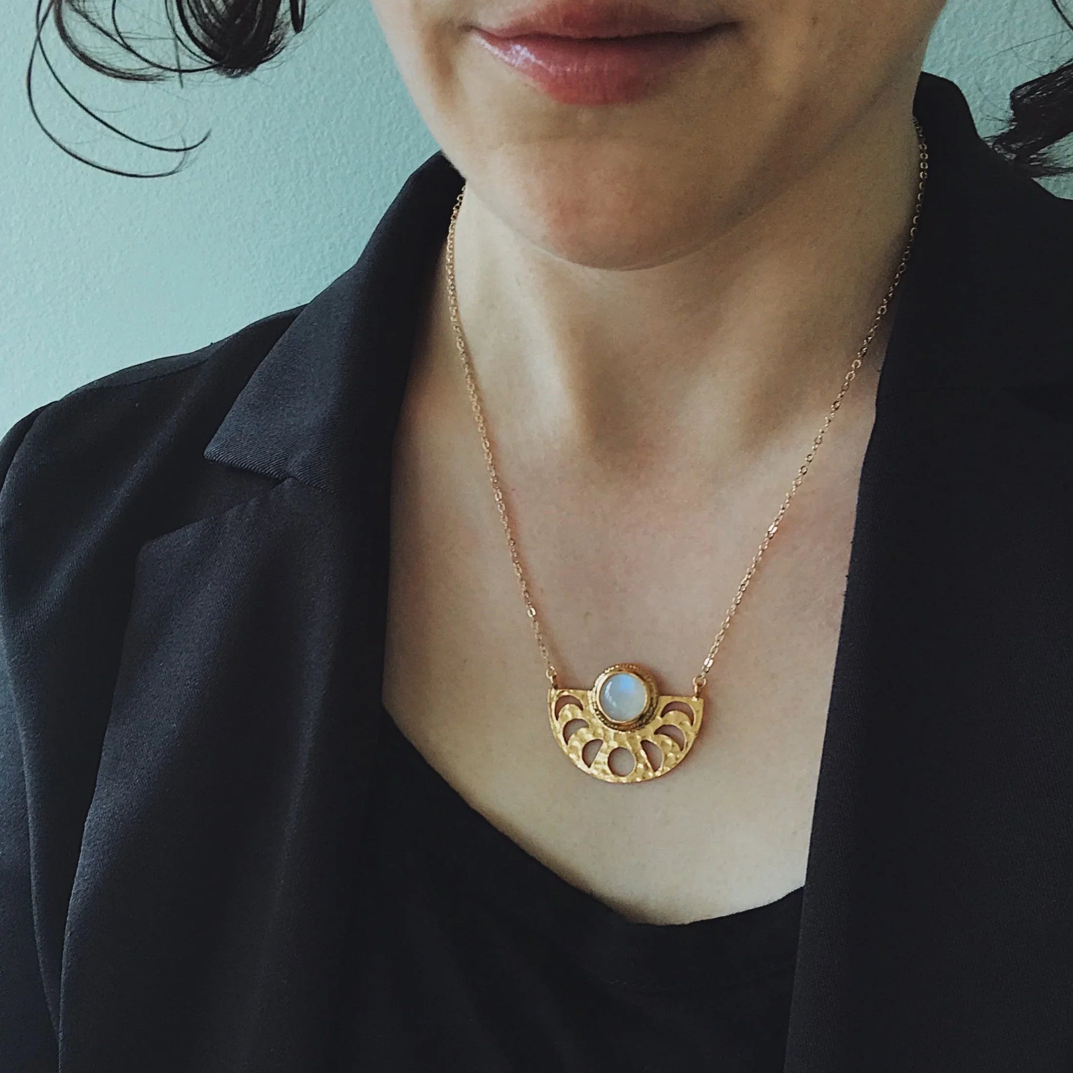 Close-up of woman wearing gold necklace with blue stone pendant and black blazer