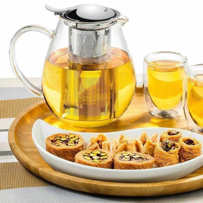 Glass teapot with herbal tea, double-walled glasses, and assorted nut pastries on wooden tray
