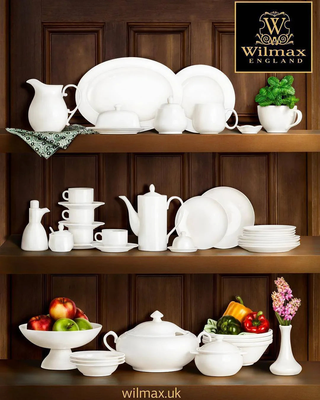 White fine china dinnerware, teapots, and cups on wooden shelves with fresh fruit and flowers.
