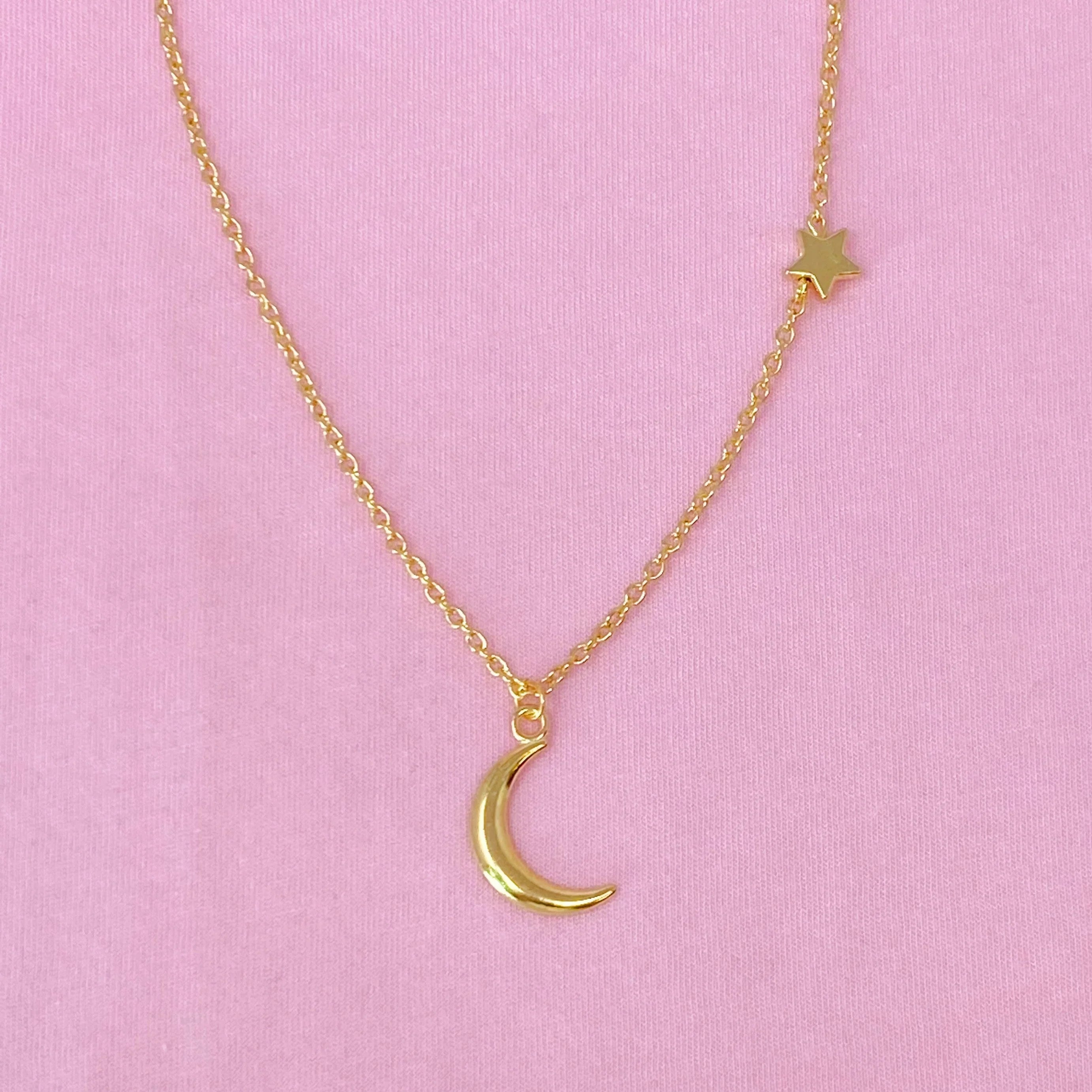 Gold chain necklace with crescent moon and star charms on pink background