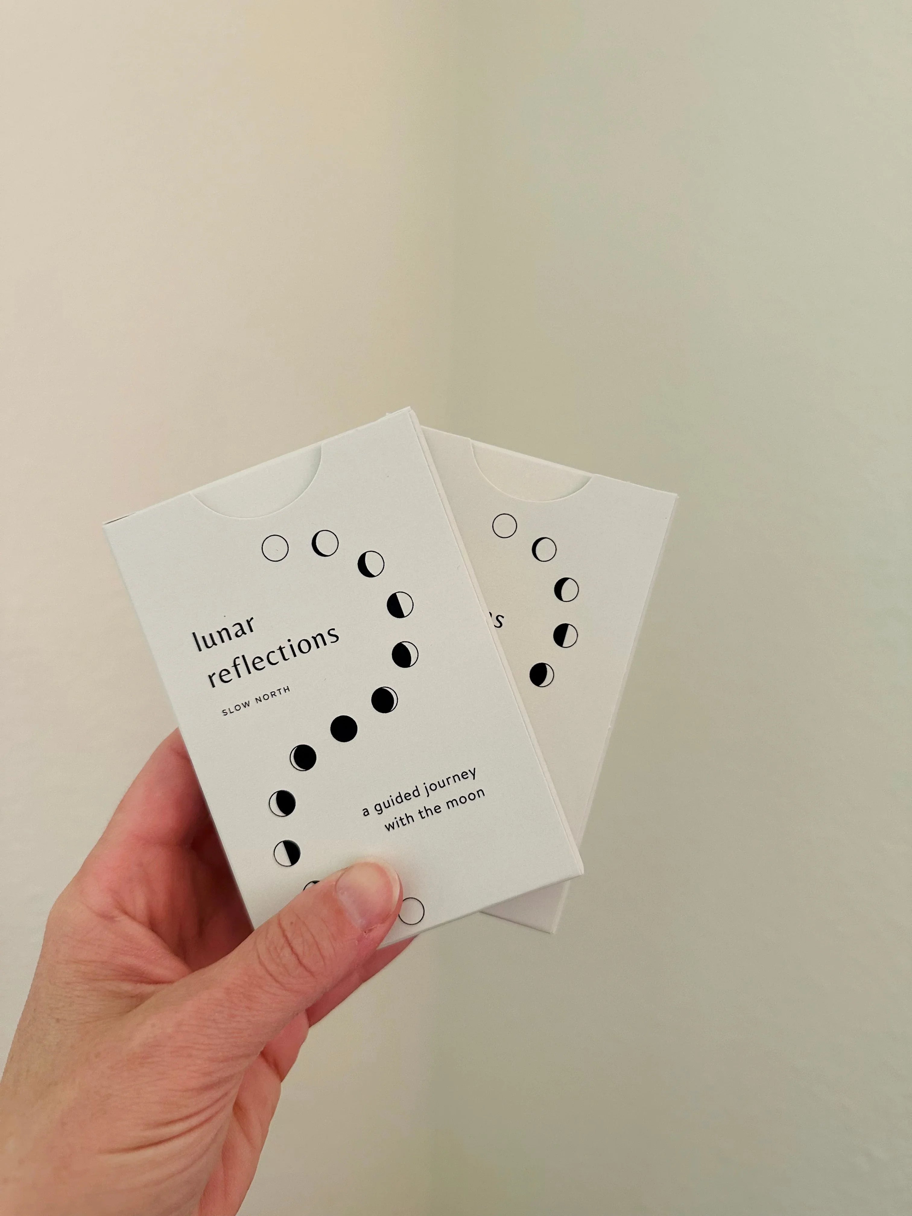 Hand holding two cards titled 'lunar reflections' with moon phase illustrations and subtitle 'a guided journey with the moon'