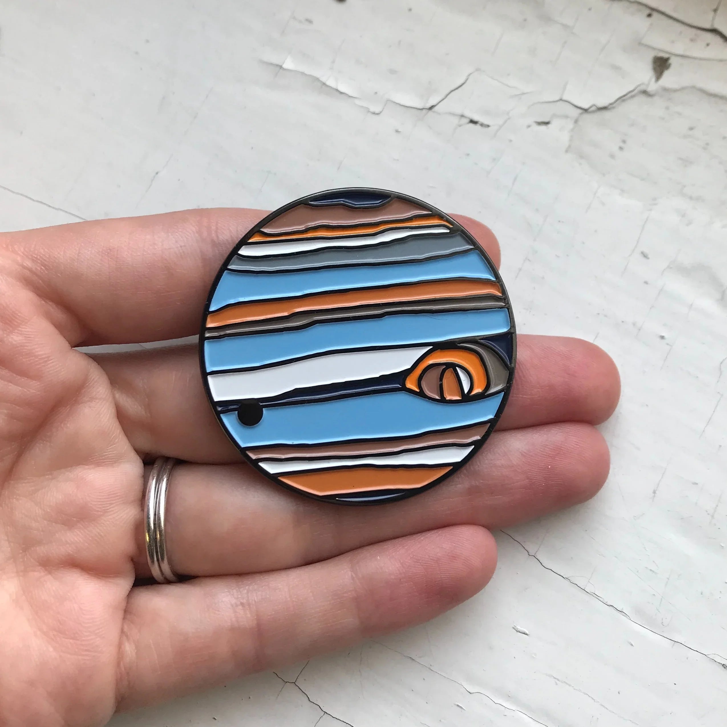 Hand holding round enamel pin with colorful cosmic planet design, Qu!rk Boutique gift accessory