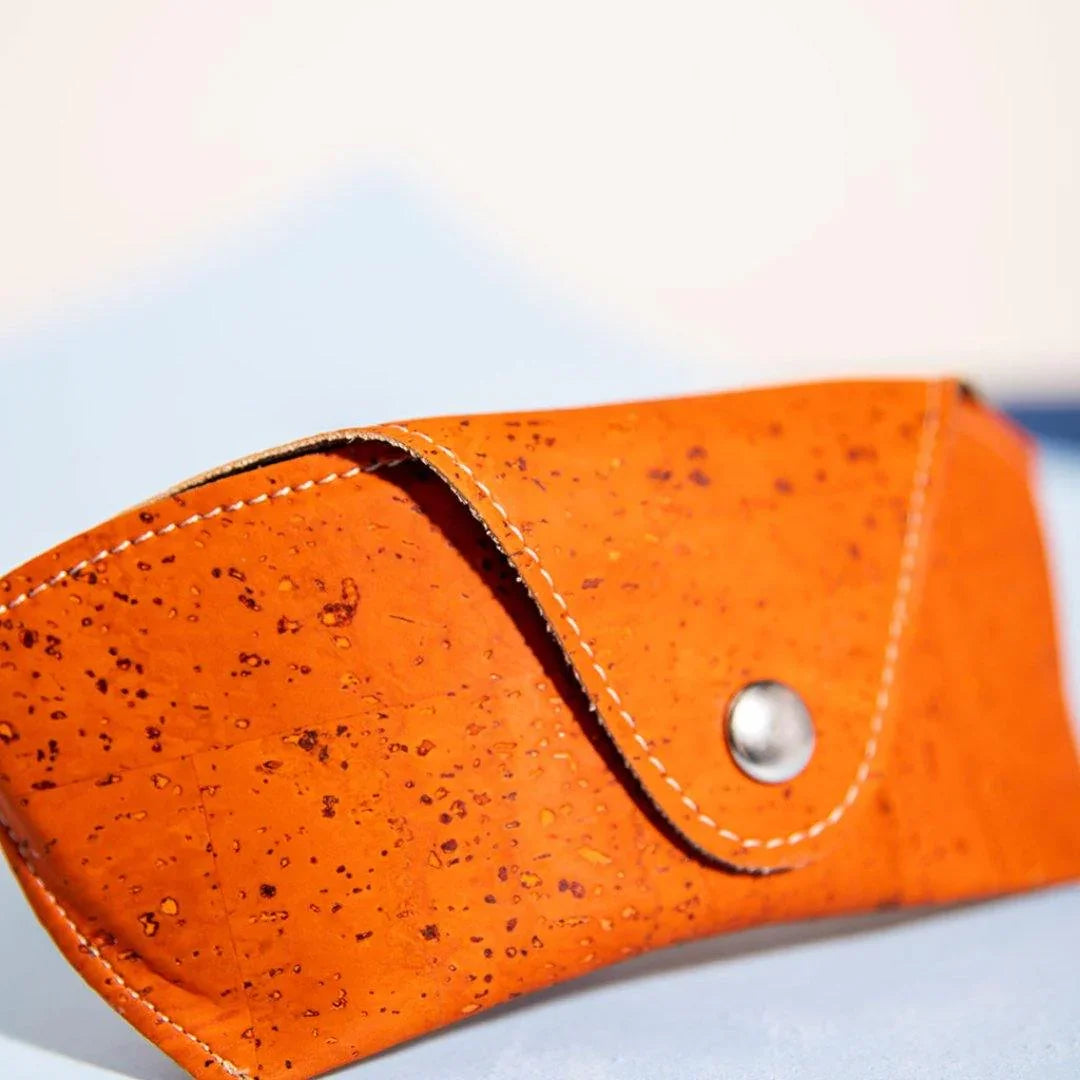 Orange cork sunglasses case with white stitching, displayed on a light pastel background
