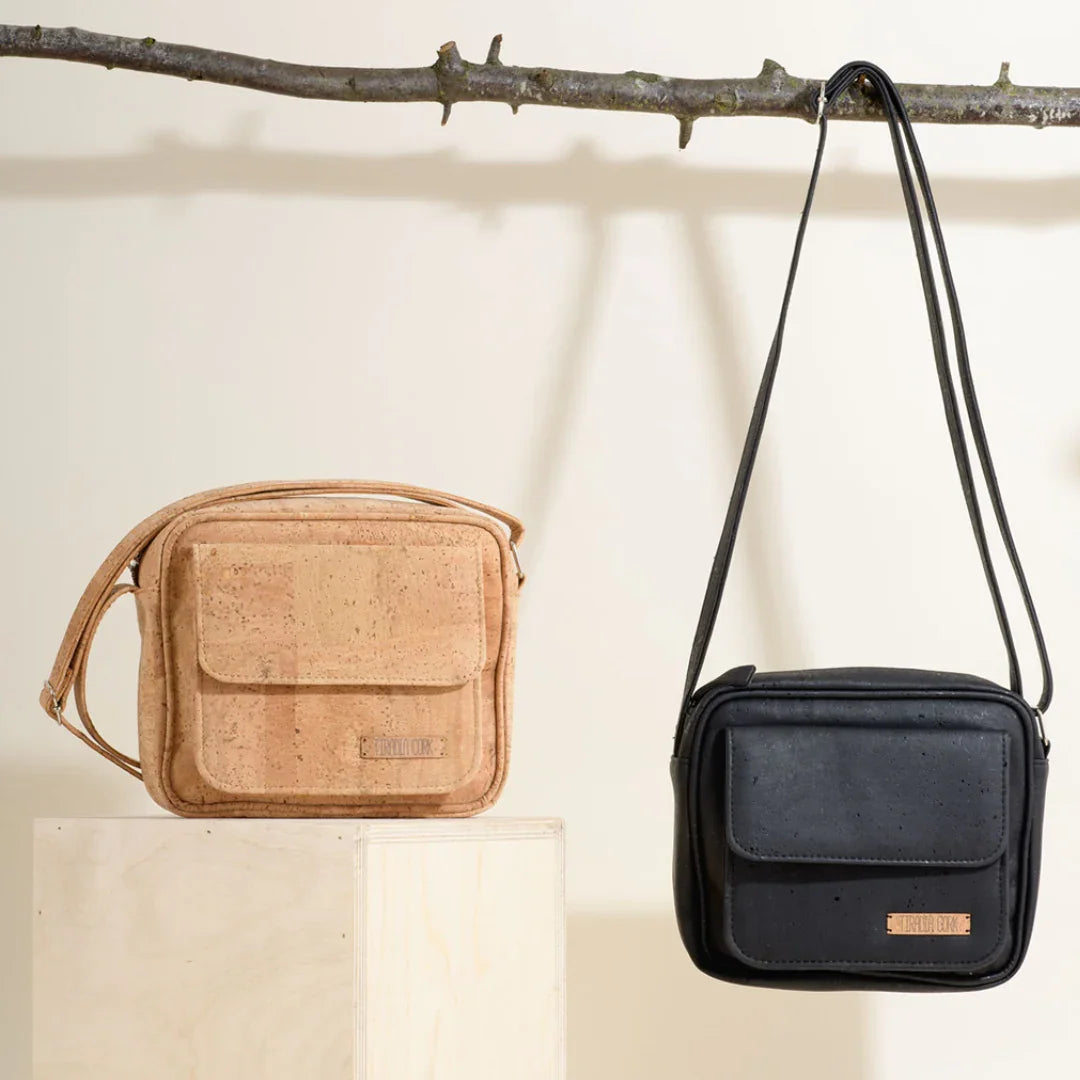 Two eco-friendly crossbody bags, one tan and one black, displayed on a branch at Qu!rk Boutique.