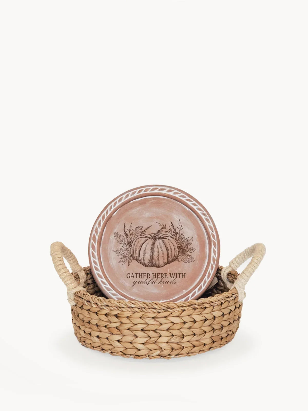 Decorative round terracotta plate with pumpkin and leaves illustration, in woven basket with rope handles