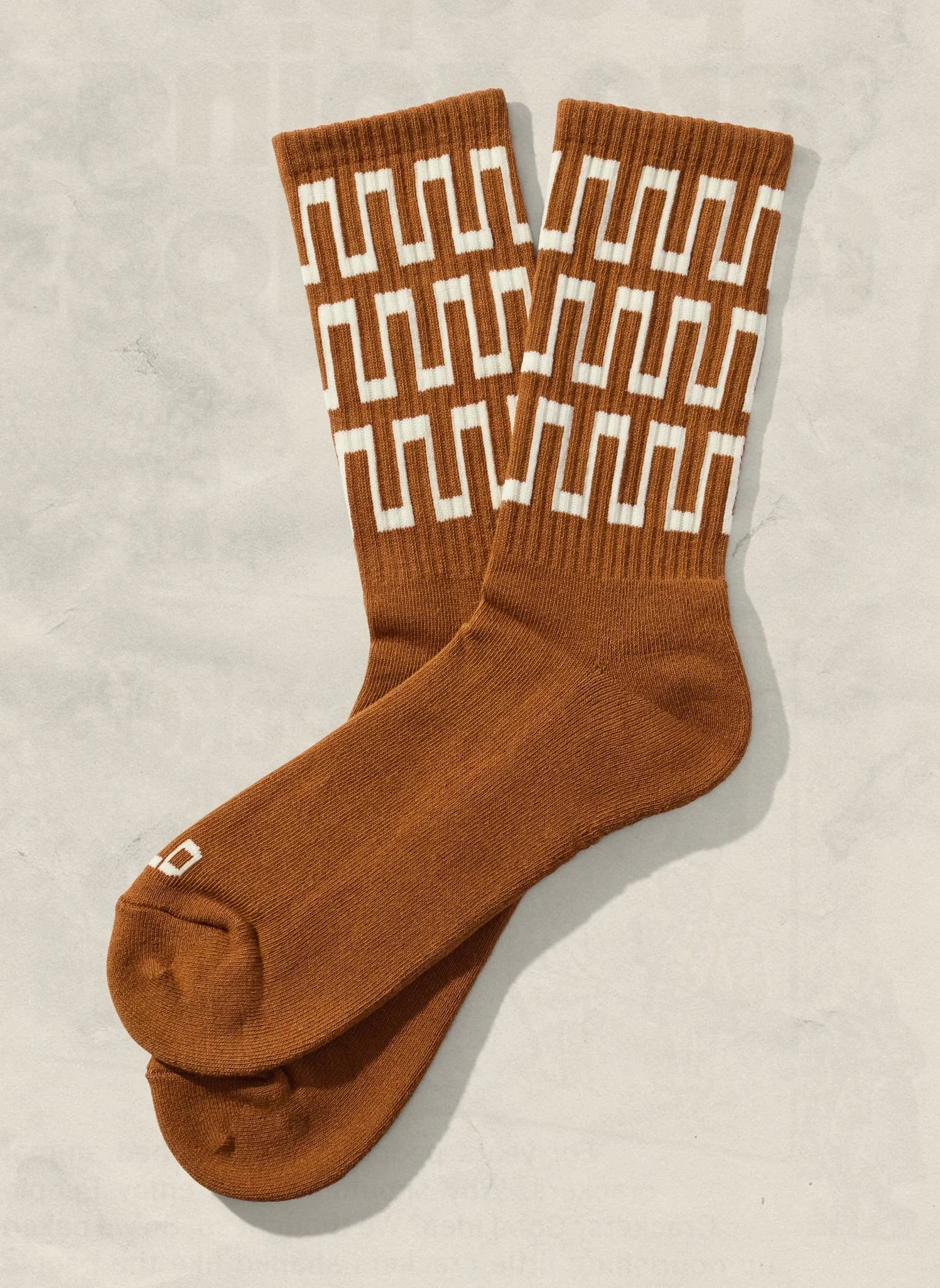 Rust brown crew socks with white geometric pattern from Qu!rk Boutique, laid flat on neutral background.