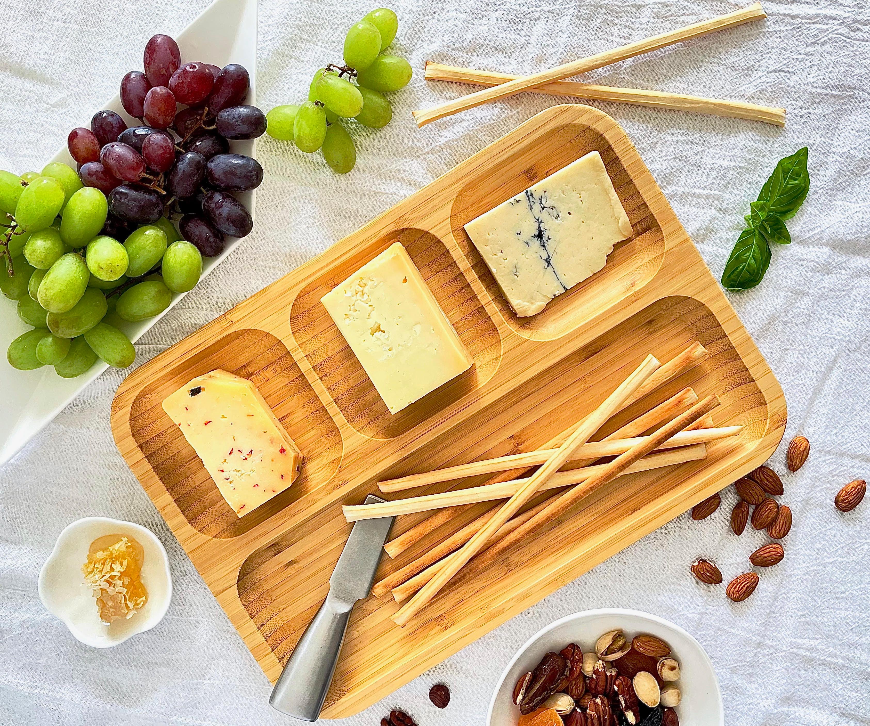 Bamboo charcuterie board with assorted cheeses, breadsticks, grapes, almonds, and honey.