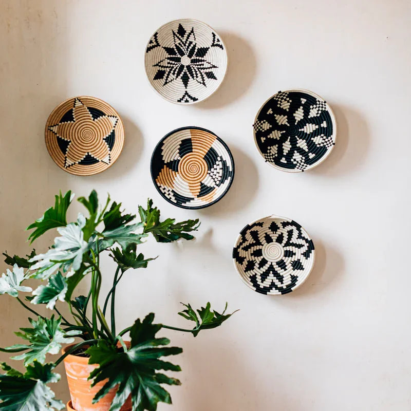 Neutral woven bowls with black and beige patterns on wall, potted plant below, Qu!rk Boutique