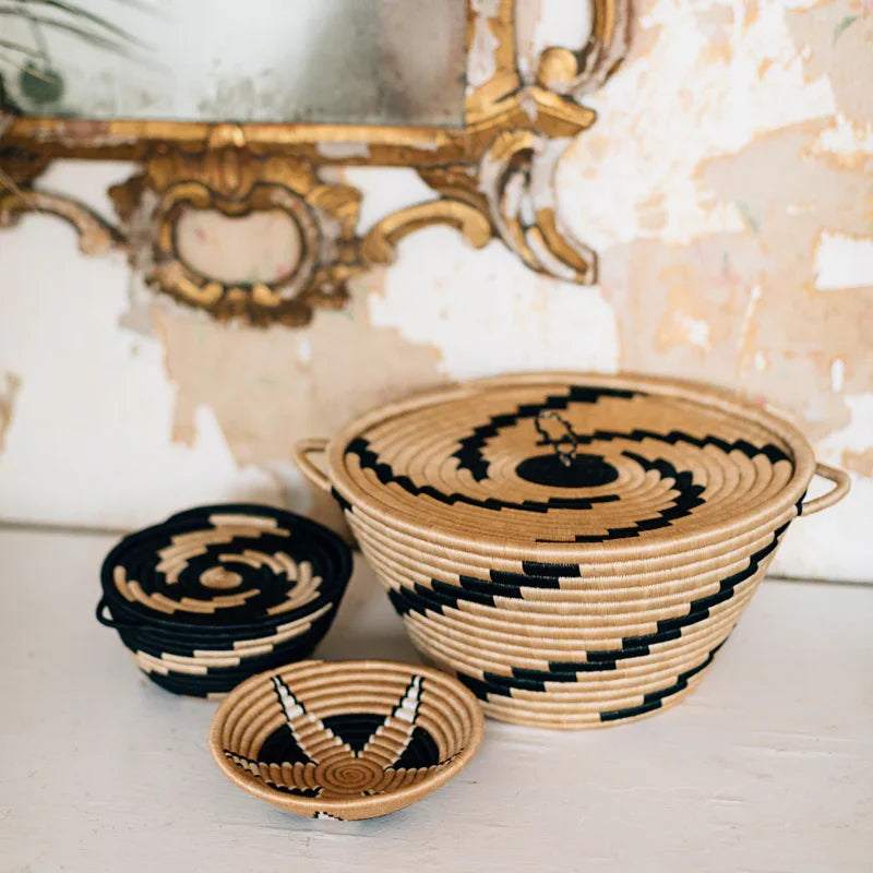 Neutral woven baskets with lids and bold black patterns, styled on a white boutique table