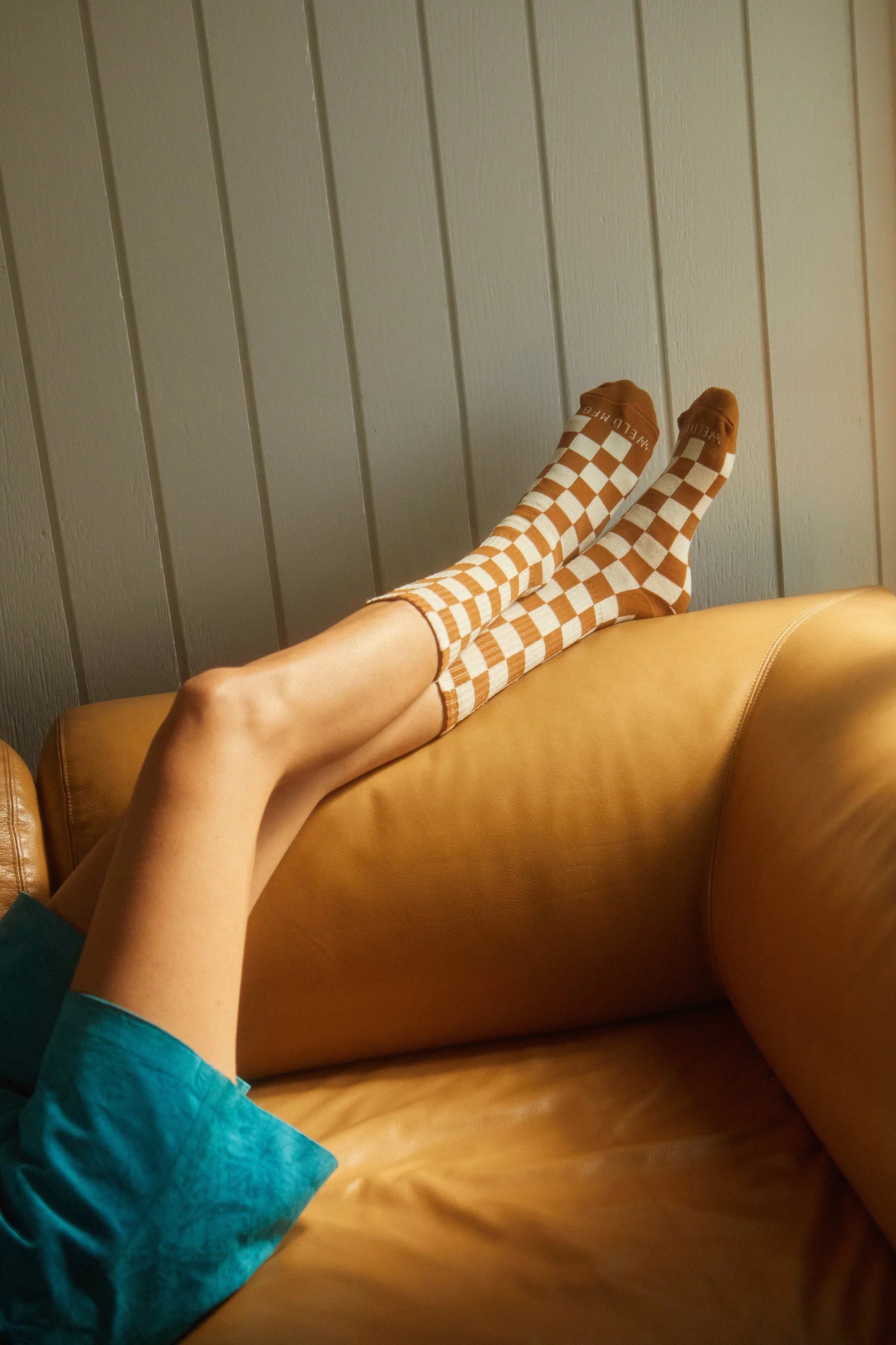 Woman relaxing on a tan couch wearing brown and white checkered socks, cozy boutique style