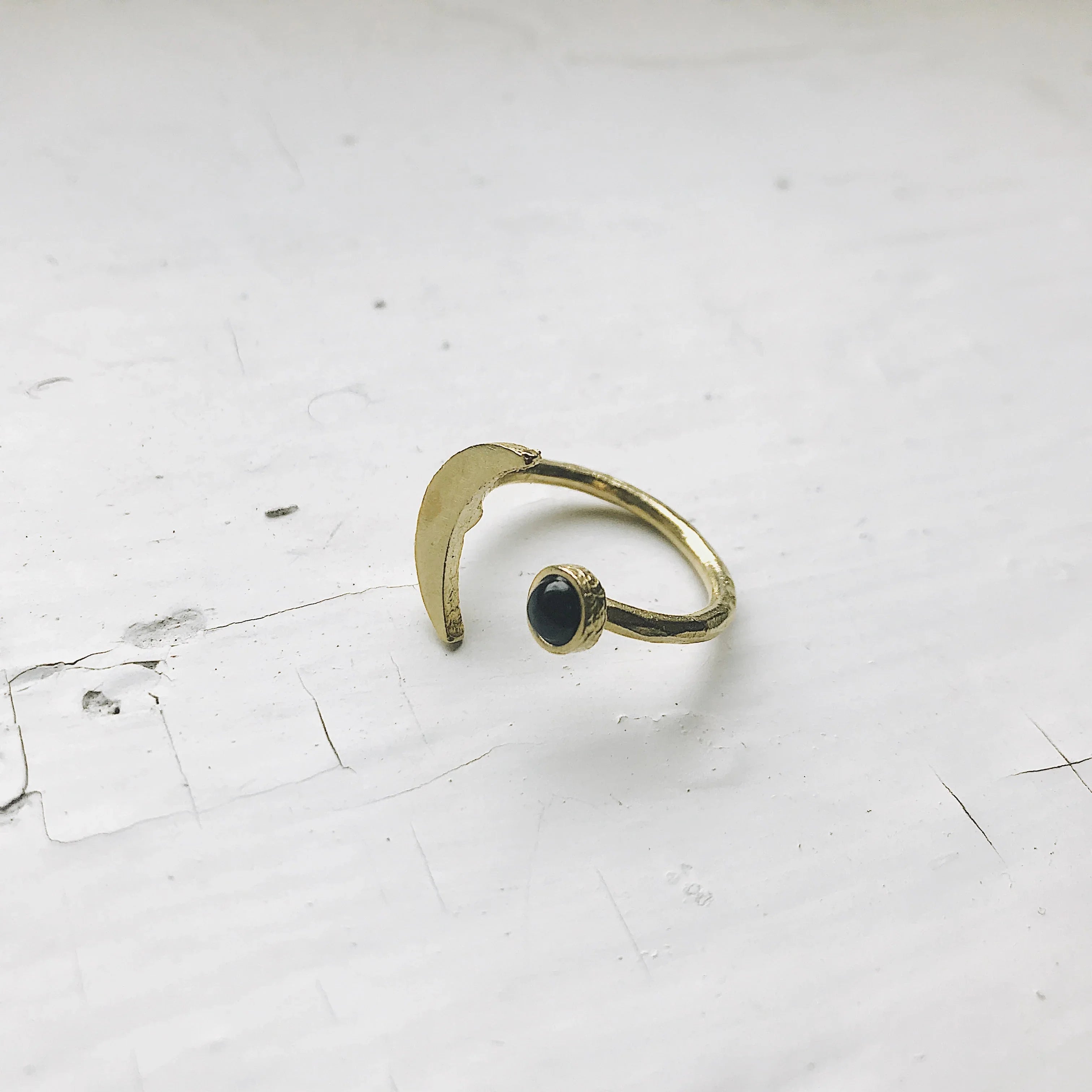 Gold open ring with crescent moon and black stone on cracked white surface