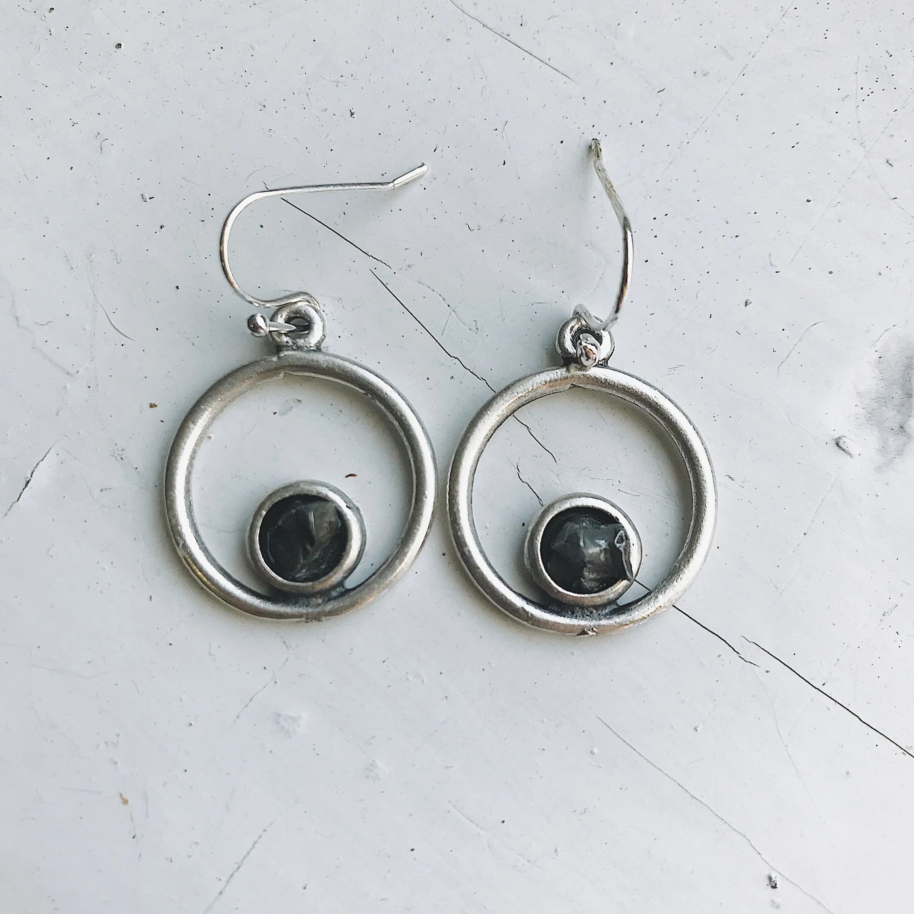 Silver hoop earrings with black circular stone in center on white textured surface