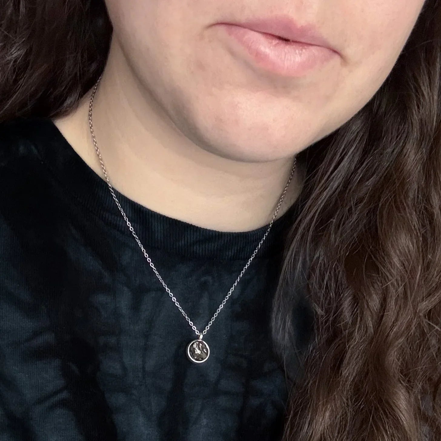 Close-up of a woman wearing a silver chain necklace with a round pendant featuring a moon and star design