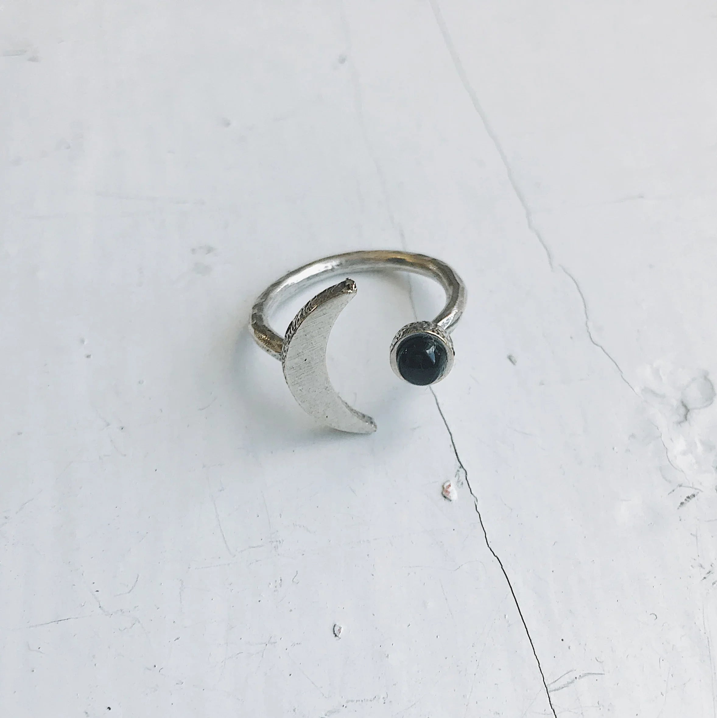 Silver open ring featuring a crescent moon and a black round stone on white textured surface
