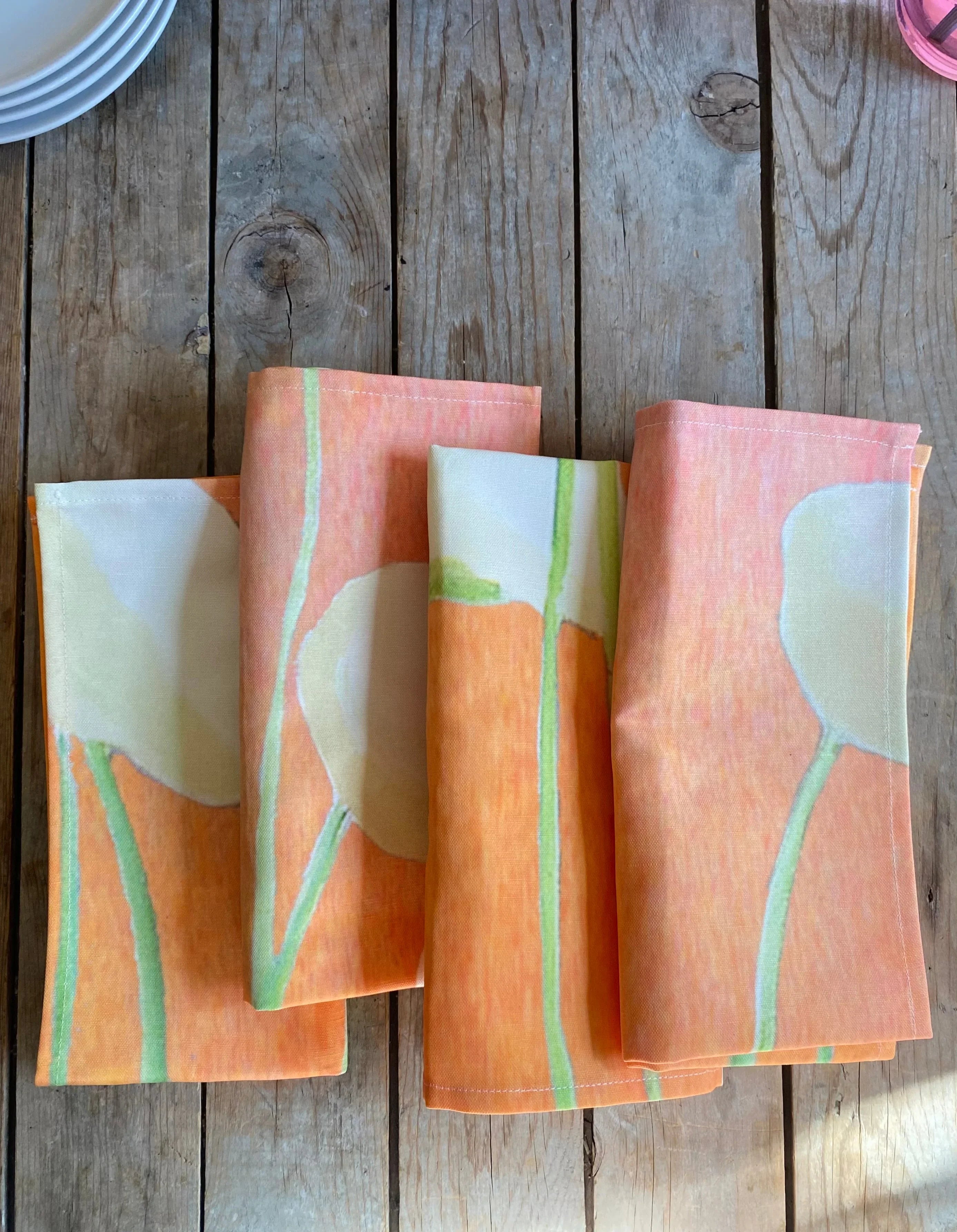Folded orange floral print fabric napkins on rustic wooden table near white plates