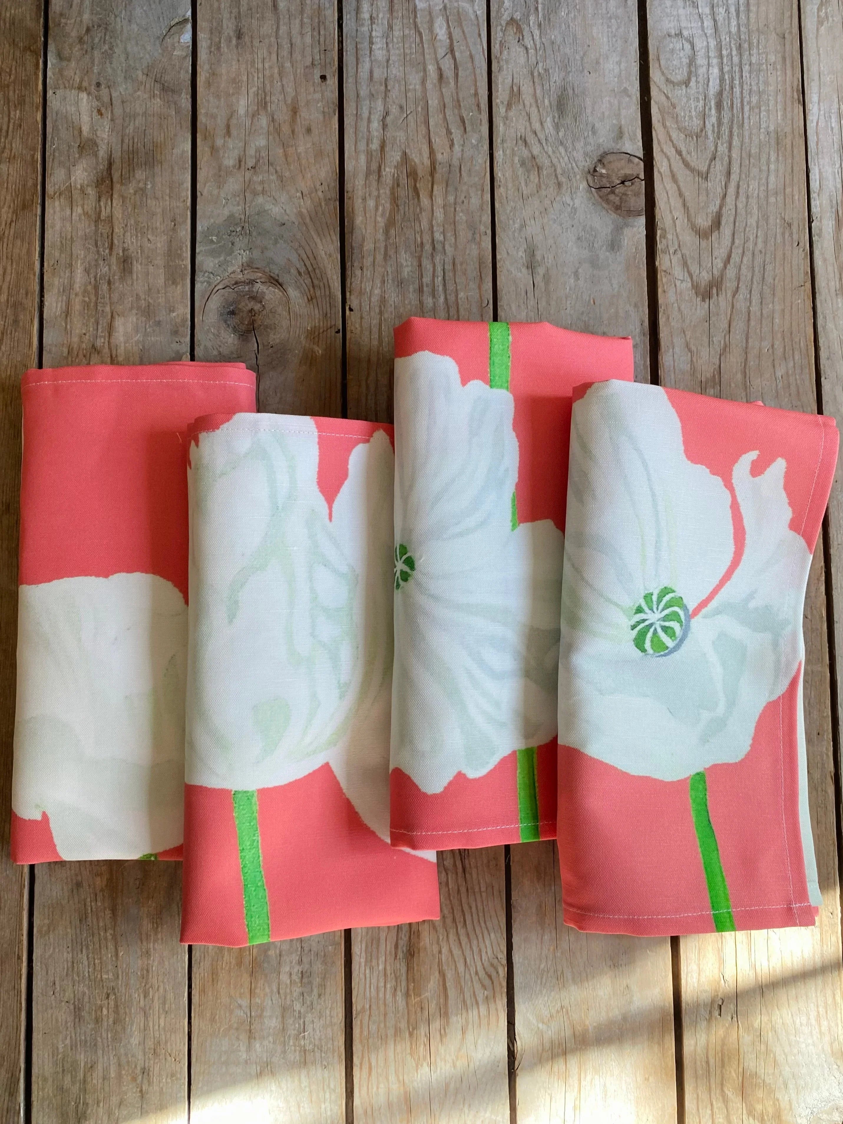 Four folded coral pink napkins with large white floral prints on rustic wooden surface