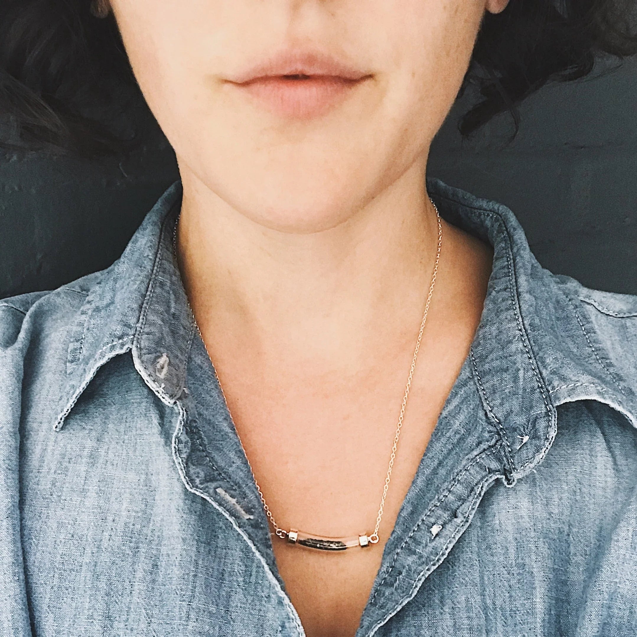 Close-up of a person wearing a blue denim collared shirt and a gold chain necklace with a curved pendant