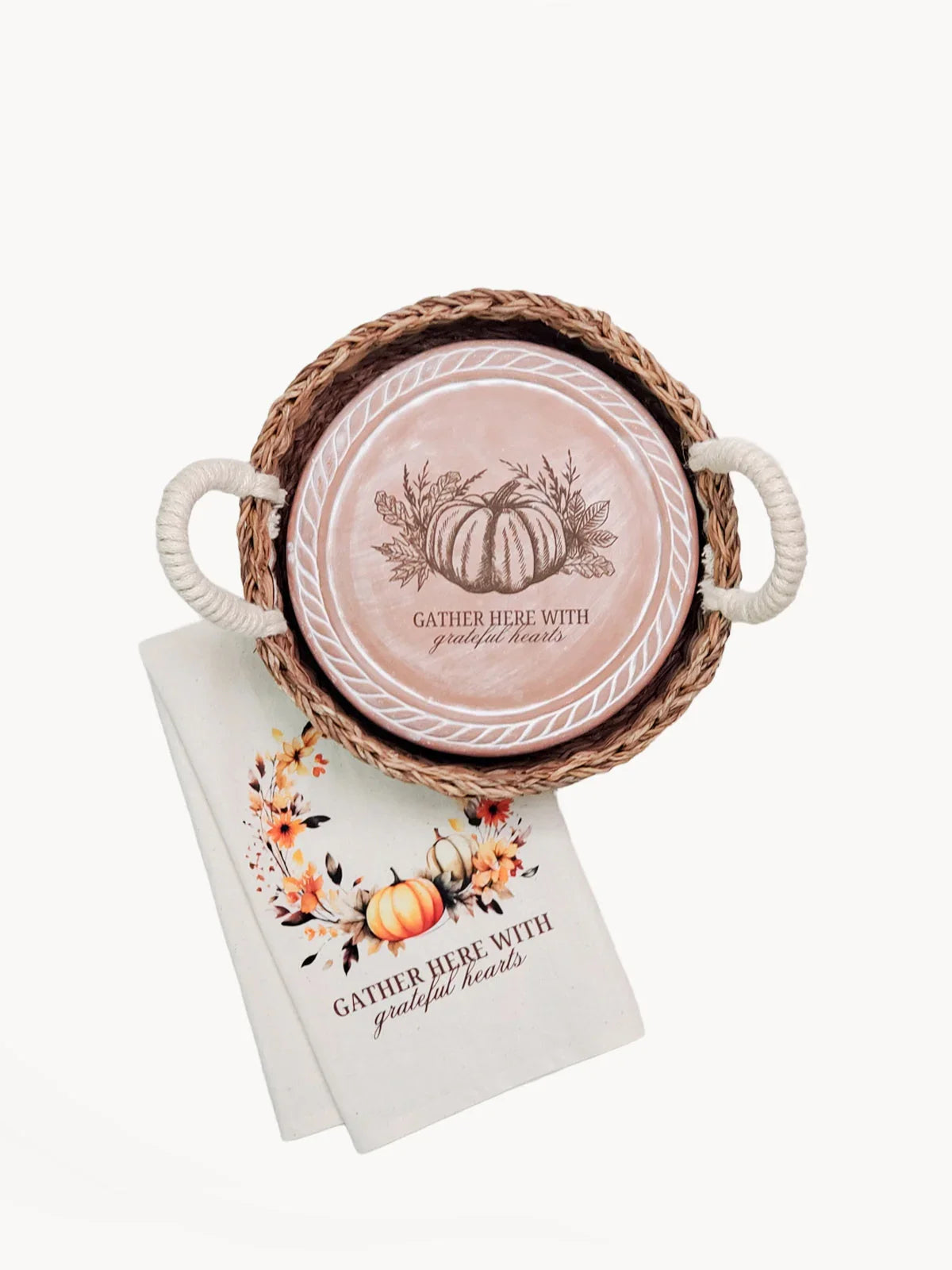 Round wicker tray with handles holding a pink plate and cloth napkin, both decorated with pumpkins and text 'Gather here with grateful hearts' for fall decor