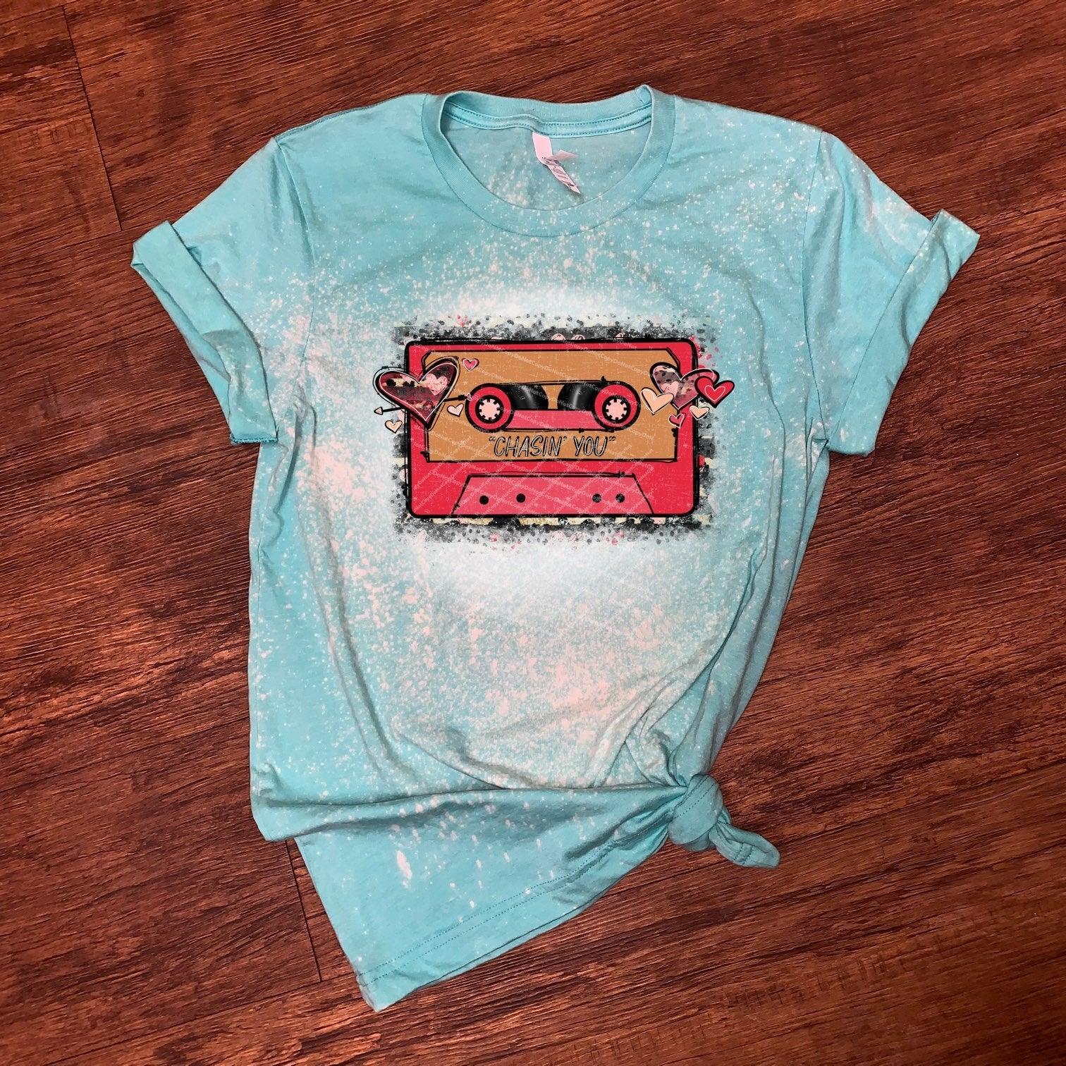 Turquoise graphic tee with retro cassette and hearts, Chasin' You text, on wood floor