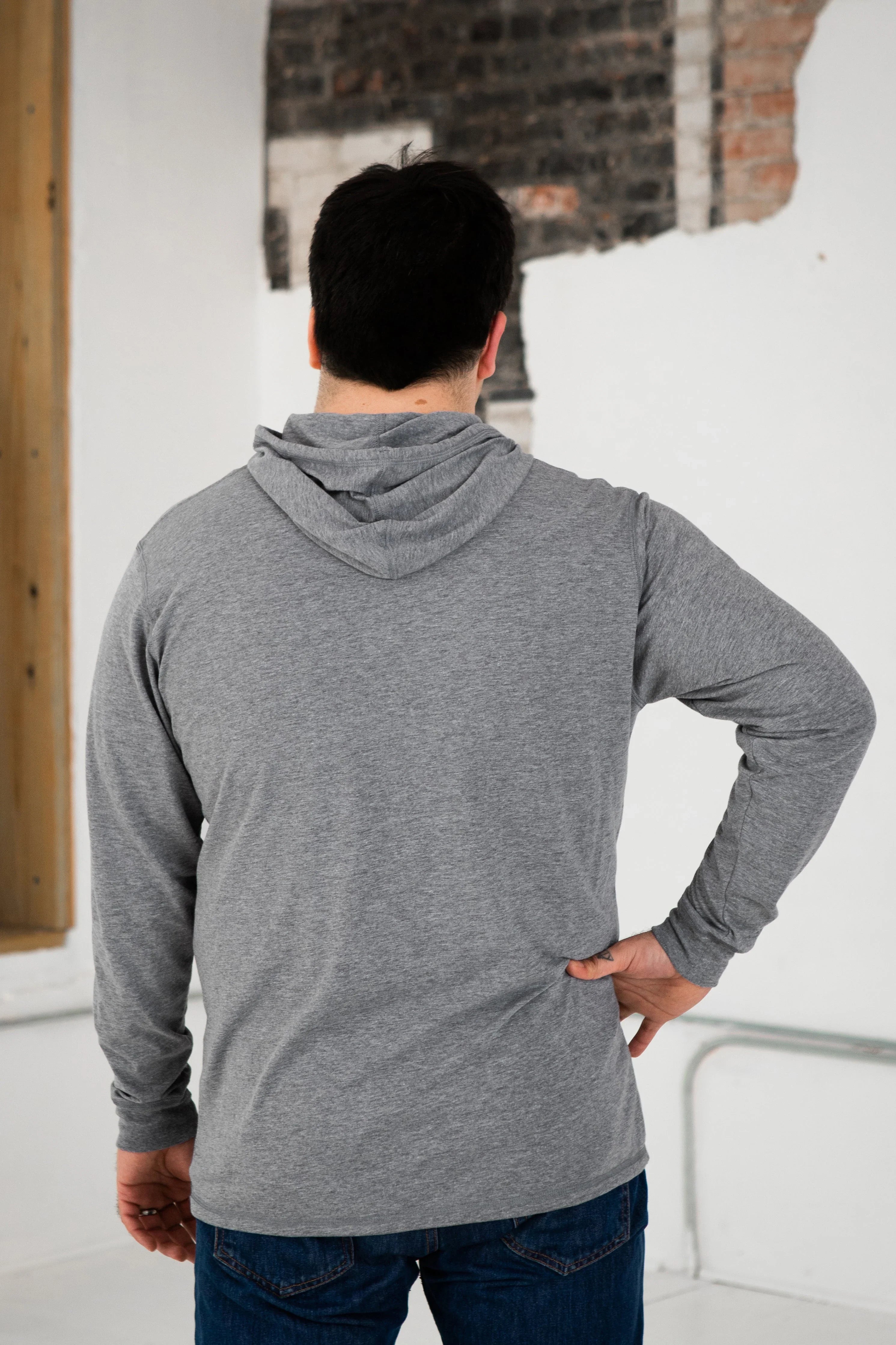 Back view of a person wearing a heather grey hoodie and jeans in a modern, rustic setting