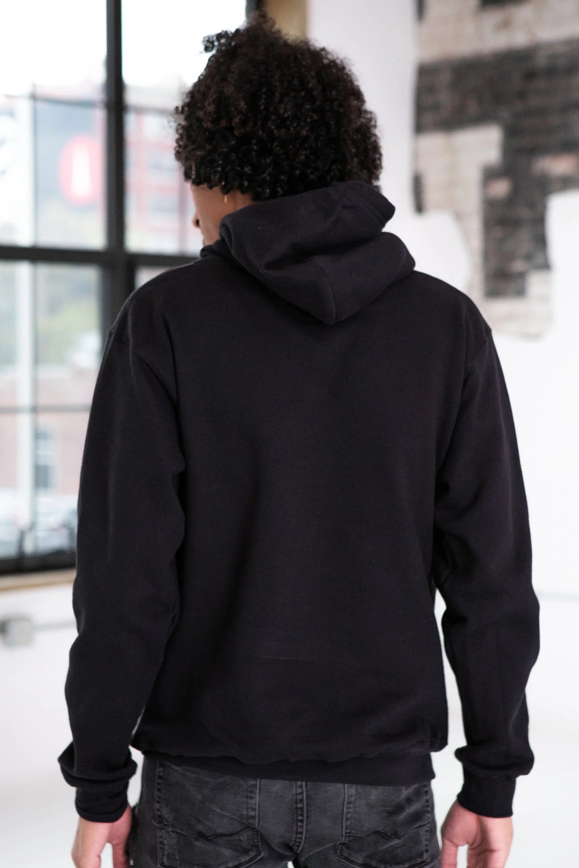Back view of model wearing black hoodie from Qu!rk Boutique in modern loft setting