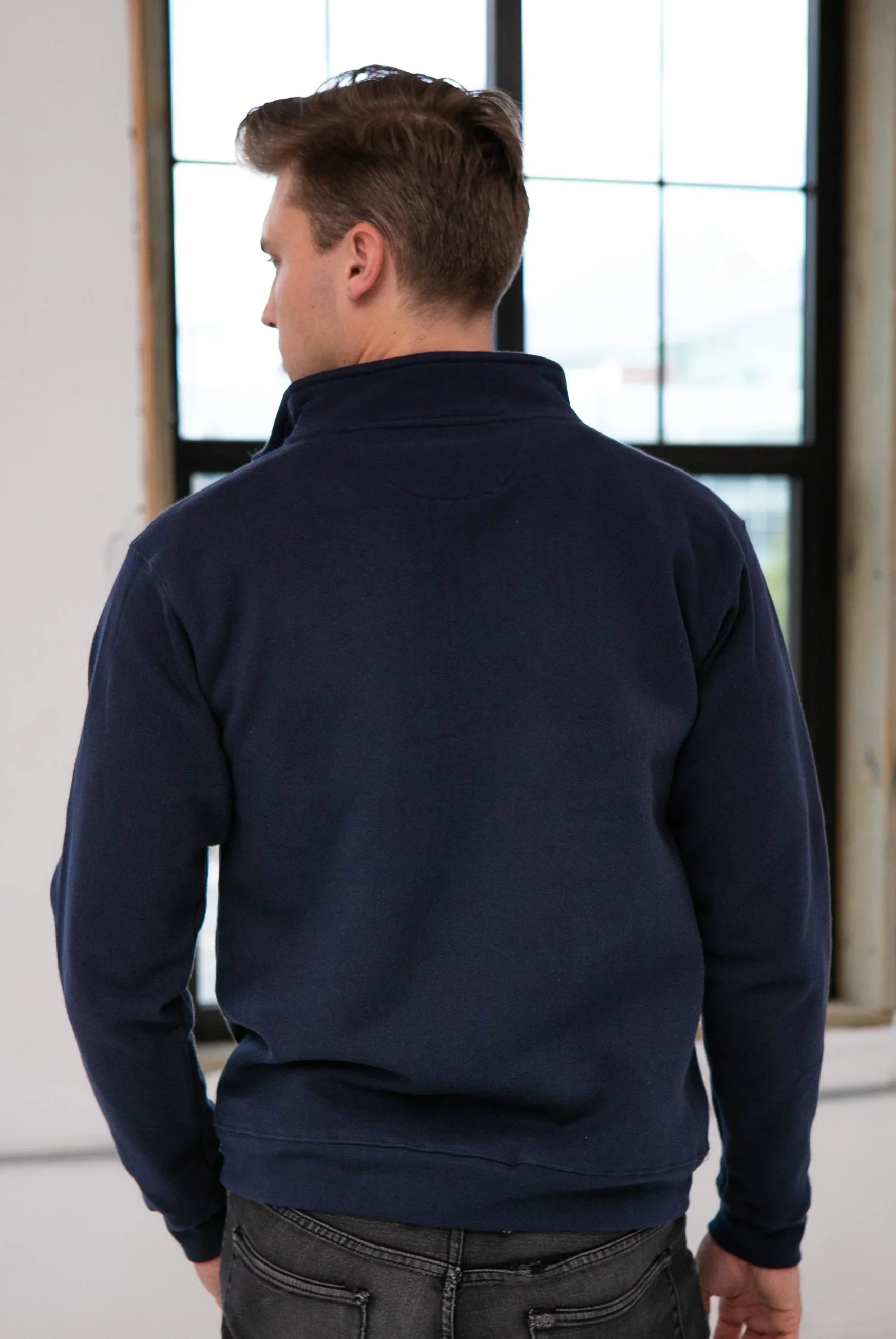 Back view of man wearing navy sweatshirt in bright boutique setting, Qu!rk Boutique