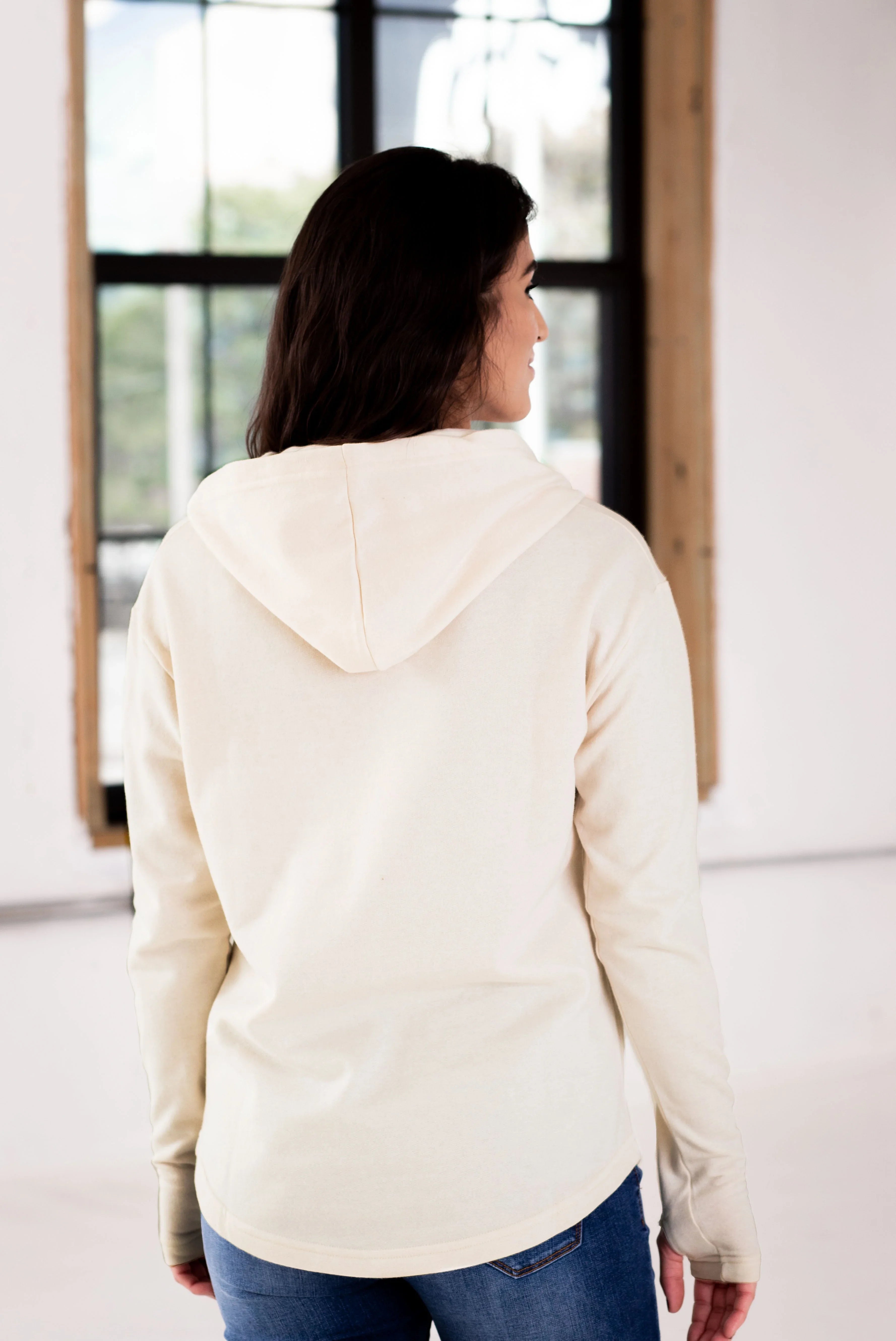 Woman in ivory hoodie and jeans, back view, in bright boutique setting at Qu!rk Boutique