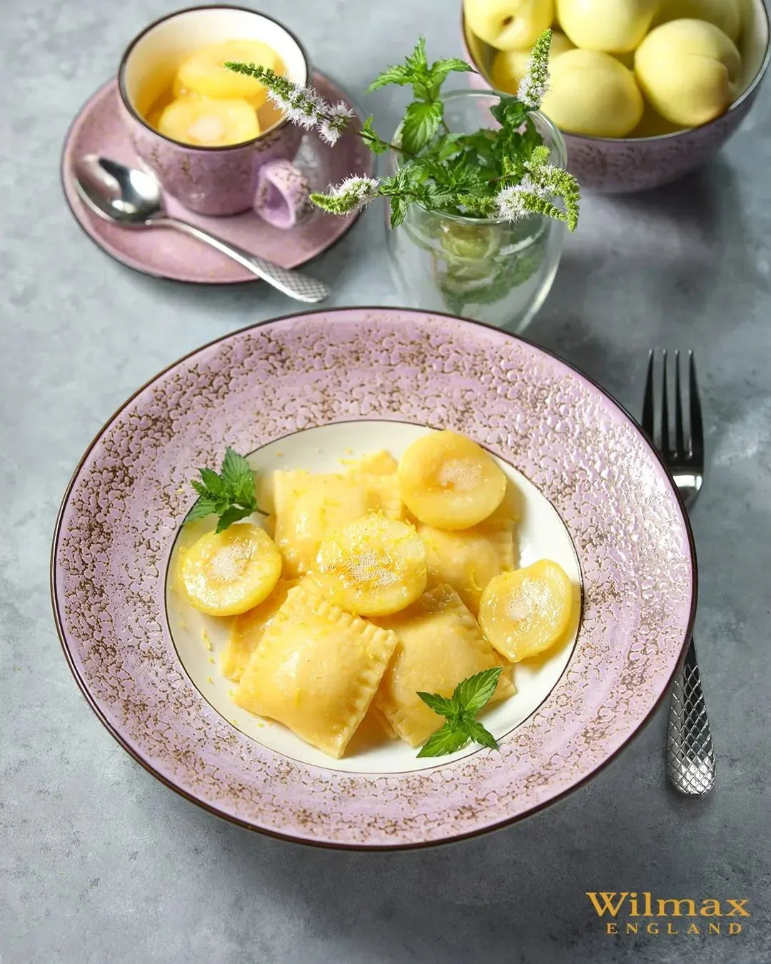 Elegant pink Wilmax England plate with ravioli and round pasta, mint garnish, teacup, and lemons, styled on a gray surface—artisan dining ware at Qu!rk Boutique & Gift Shop.