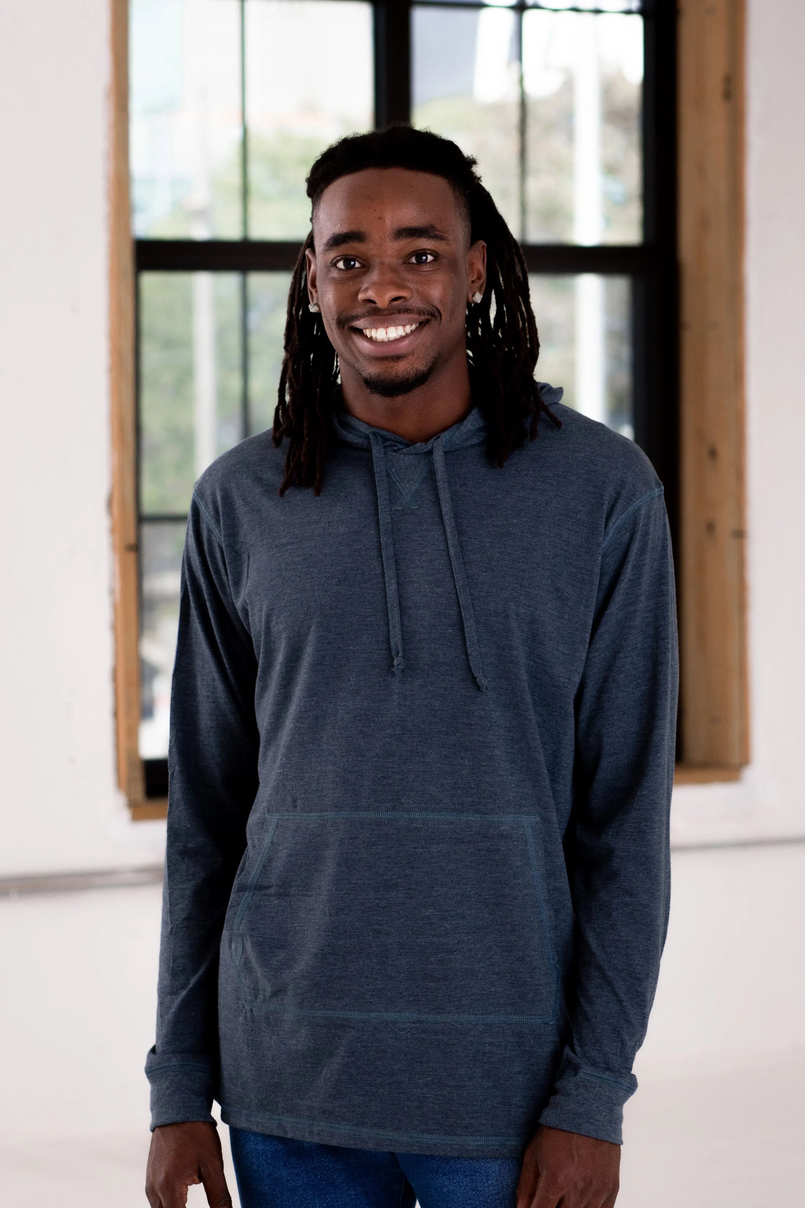 Smiling man modeling a navy hooded pullover in a bright boutique setting at Qu!rk Boutique.